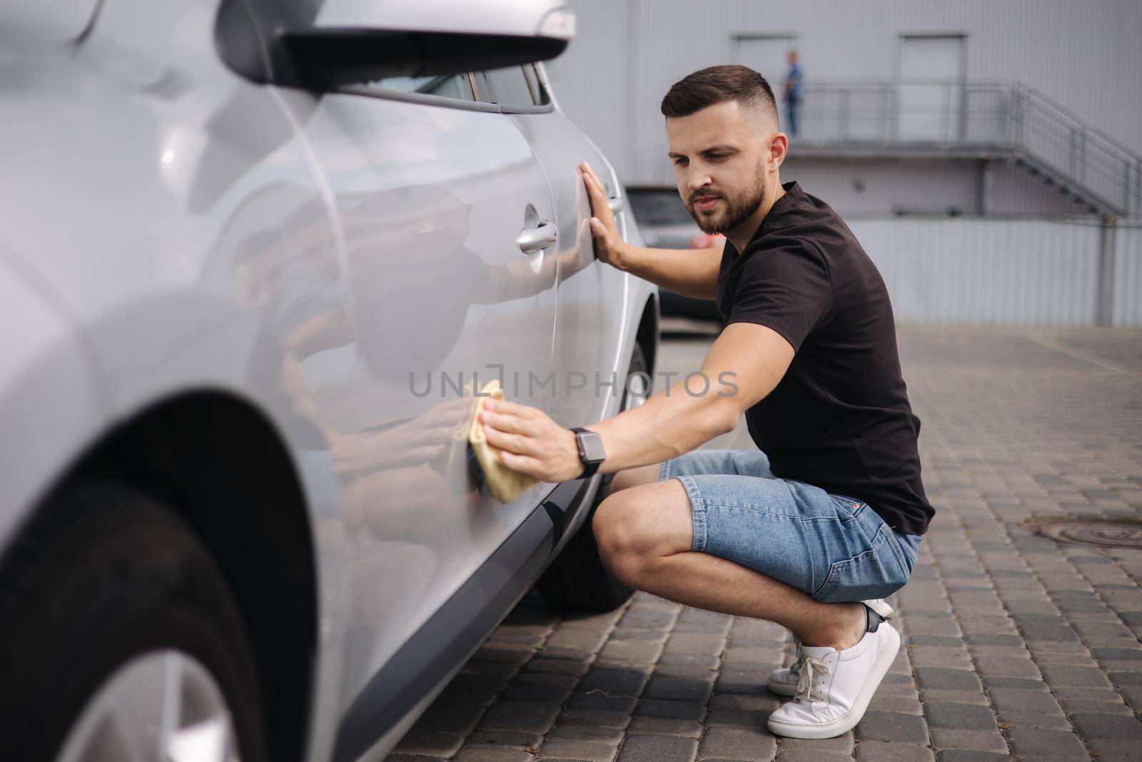 Handsome man wipes a car with a rag in a showroom at a self-service car wash. Gray car. Polished car with hard wax.