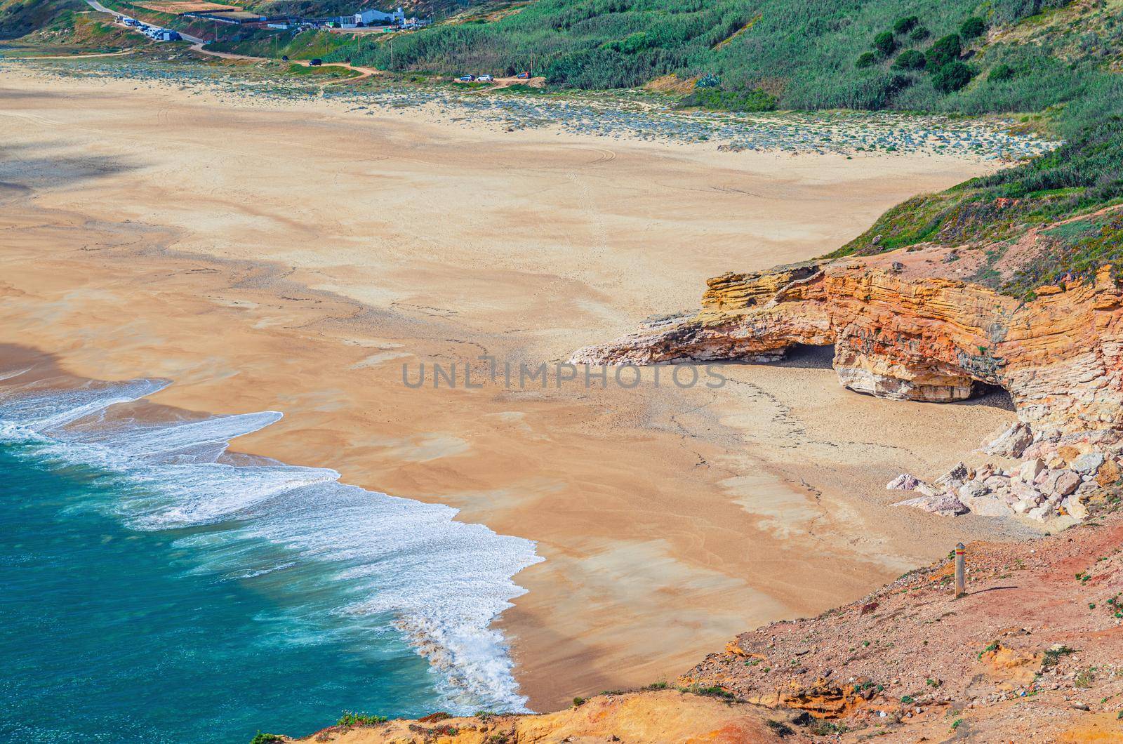 Top aerial view of sandy beach with rocks and cliffs and waves of azure turquoise water of Atlantic Ocean near Nazare town, North beach Praia do Norte, Leiria District, Oeste region, Portugal