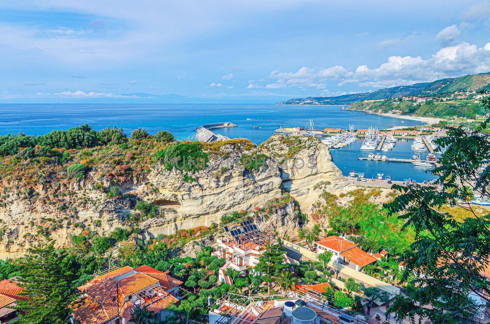 Tropea town aerial view of port marina, stone rocks and cliffs and Tyrrhenian sea with turquoise water and mountains in horizon, Vibo Valentia, Calabria, Southern Italy