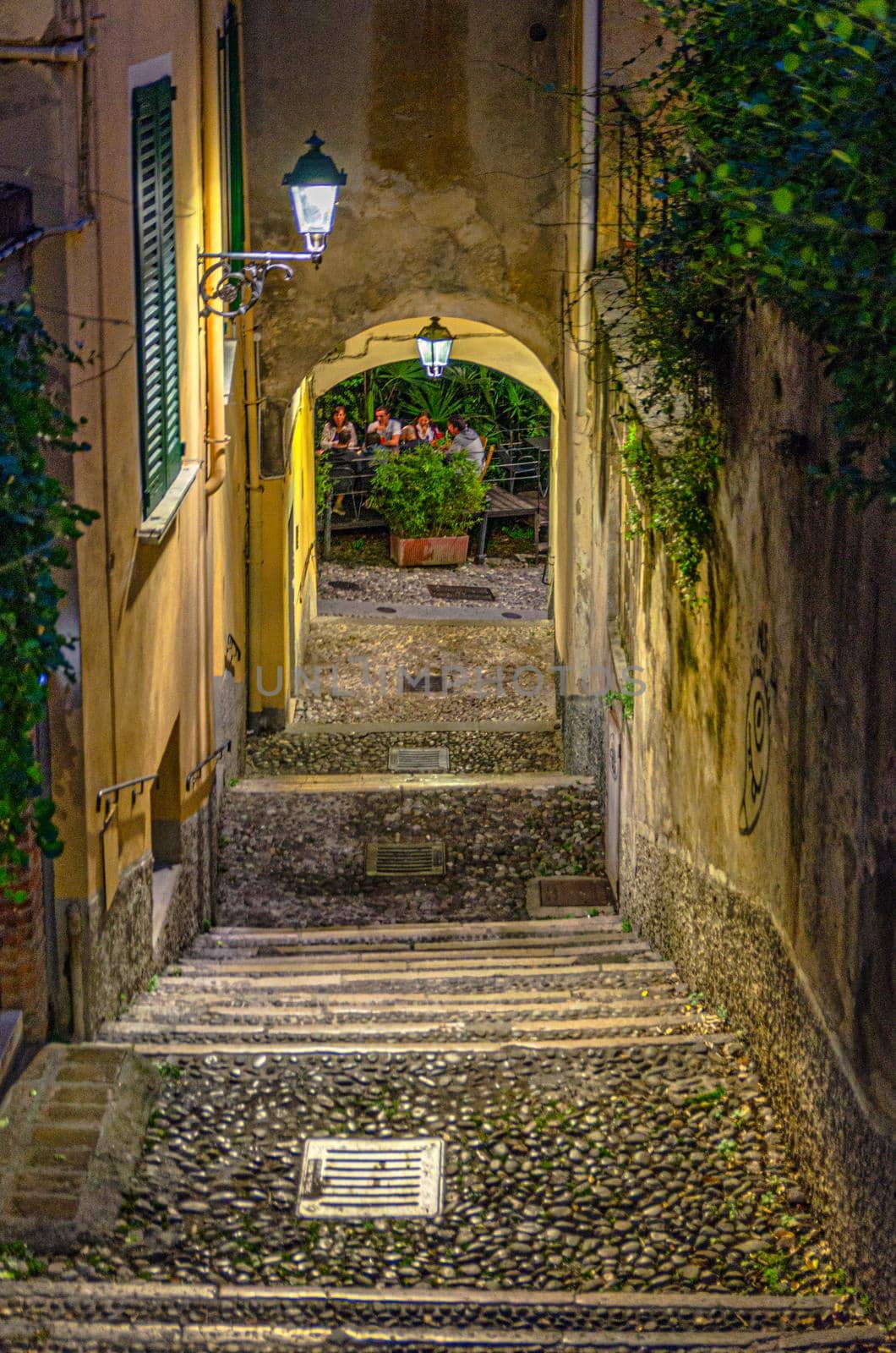 Cobblestone staircase with stairs, green trees and bushes, street lights between stone walls in Brescia city historical centre, night evening vertical view, Lombardy, Northern Italy