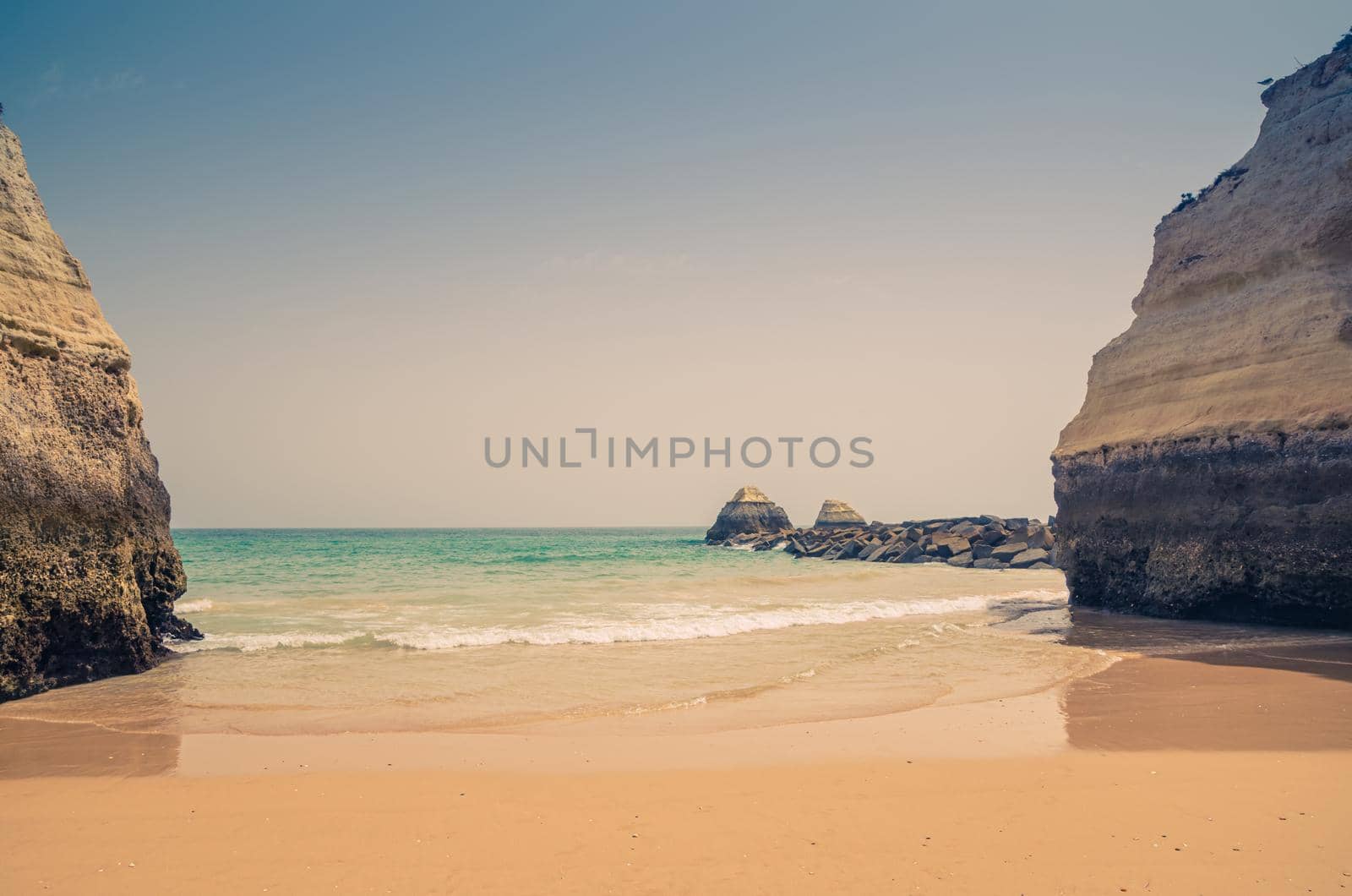 Landscape of beautiful sandy beach Praia dos Tres Castelos with rocks and cliffs in Portimao town, Algarve district, turquoise water of Atlantic Ocean in sunny day, blue sky background, Portugal