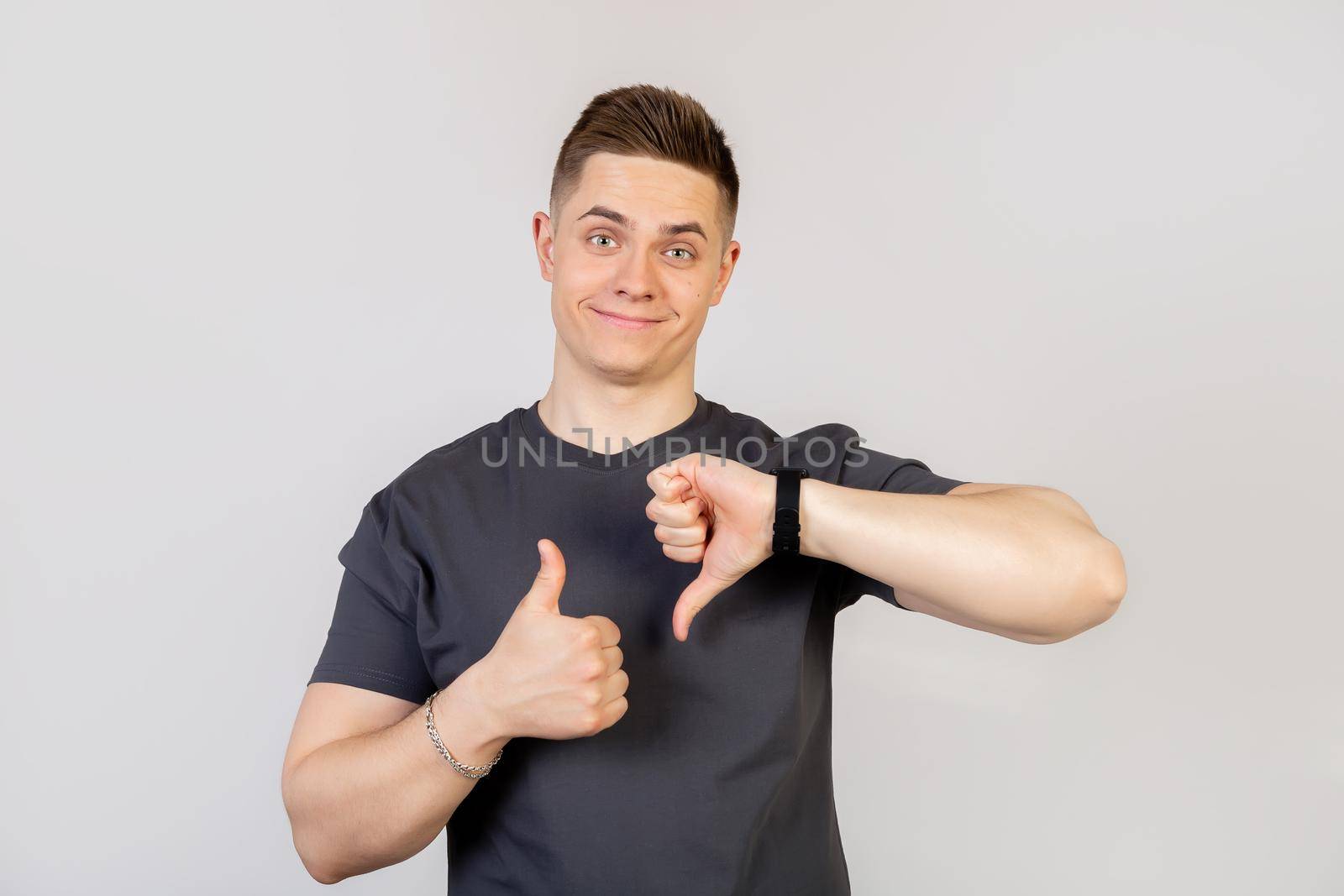 The guy shows a finger up and down gesture. Young handsome man on an isolated background. Do thumbs up and down, disagreement and expression of agreement. Crazy conflict