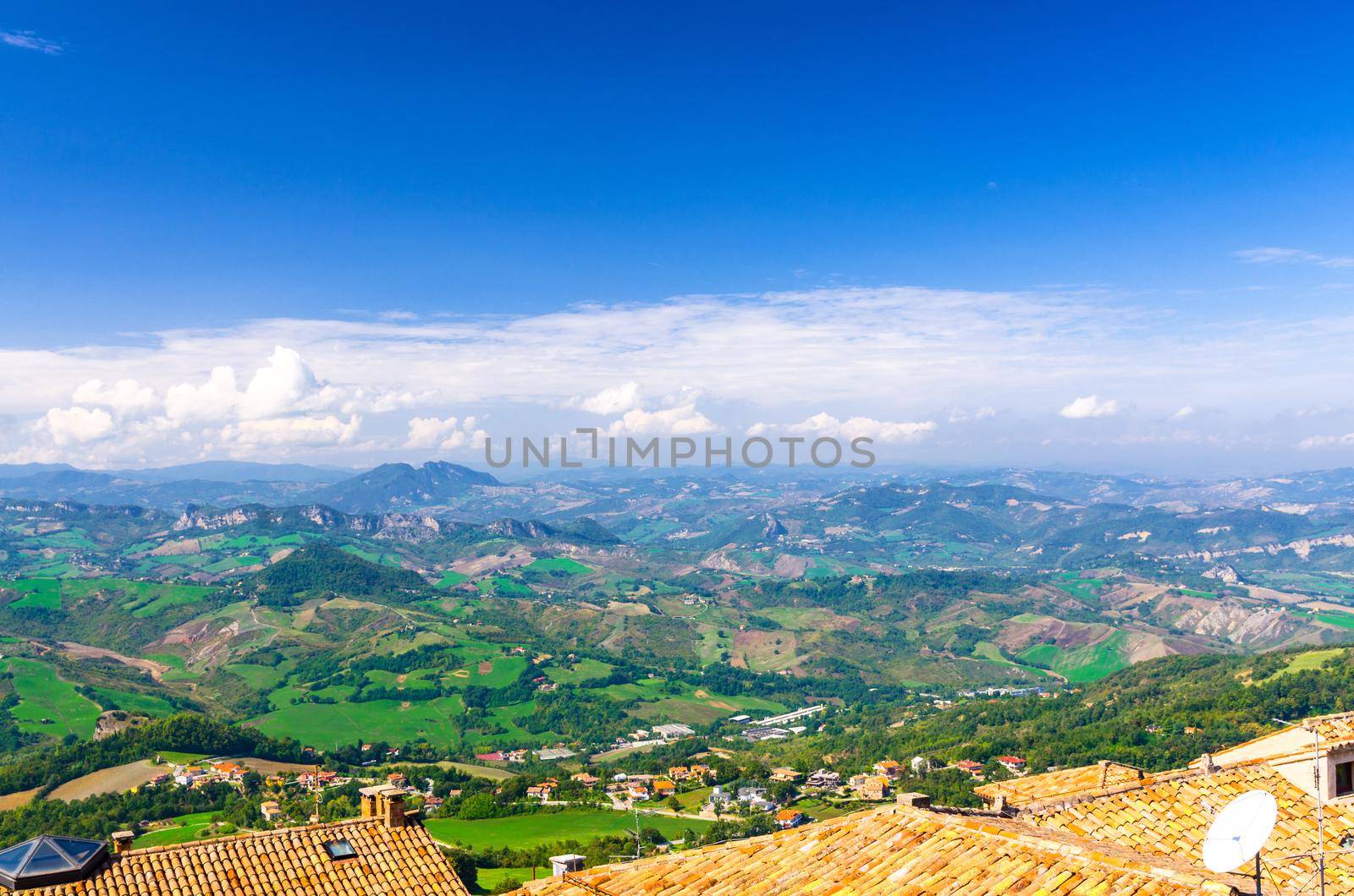 Aerial top panoramic view of landscape with valley, green hills, fields and villages of Republic San Marino suburban district with blue sky white clouds background. View from San Marino fortress