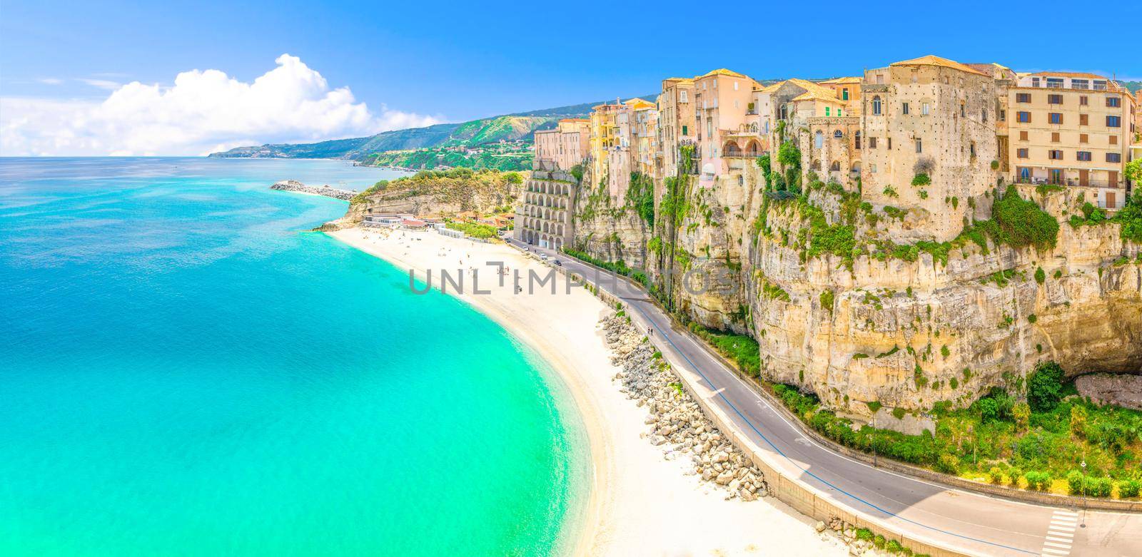 Aerial panoramic view of Tropea town and beach coastline of Tyrrhenian Sea with turquoise azure water, colorful houses buildings on top of high big rocks, road along sea, Calabria, Southern Italy