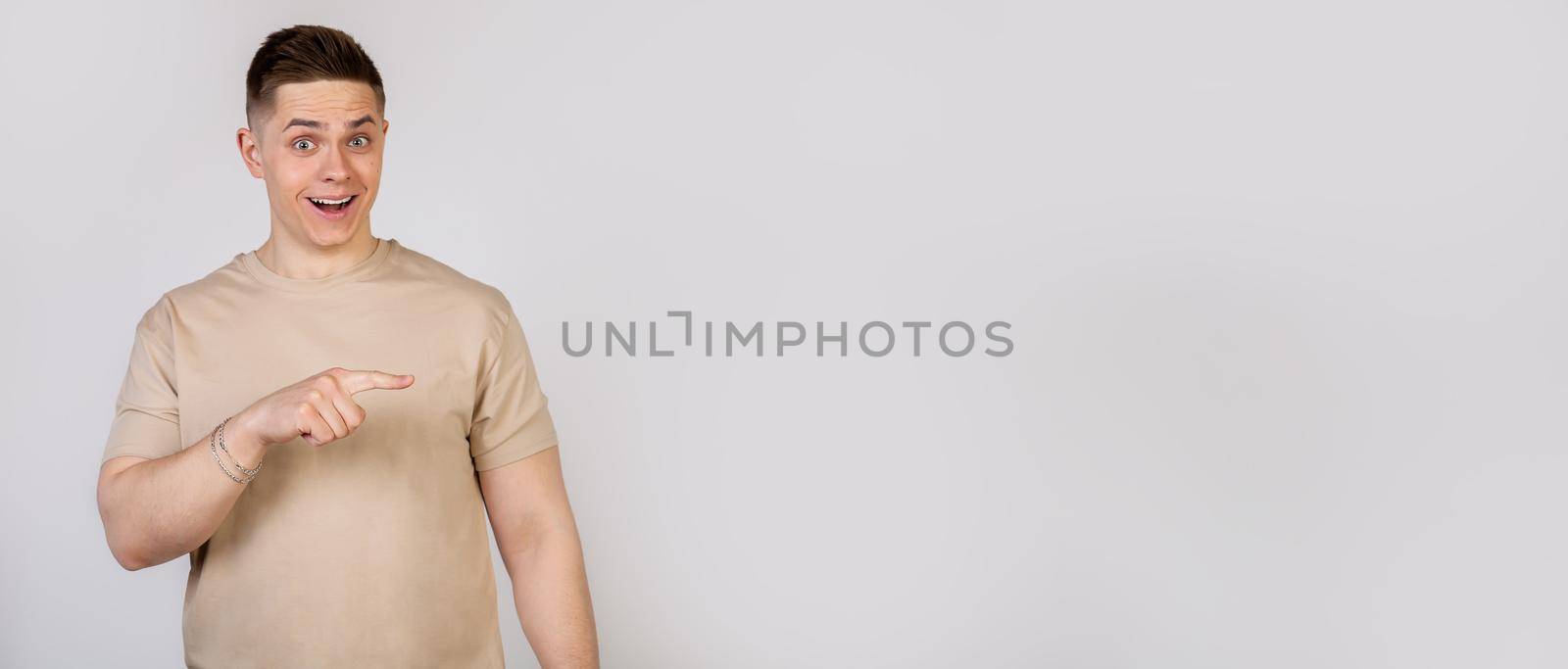Handsome strong young man pointing finger to the right with a surprised expression on his face. Copy ad space