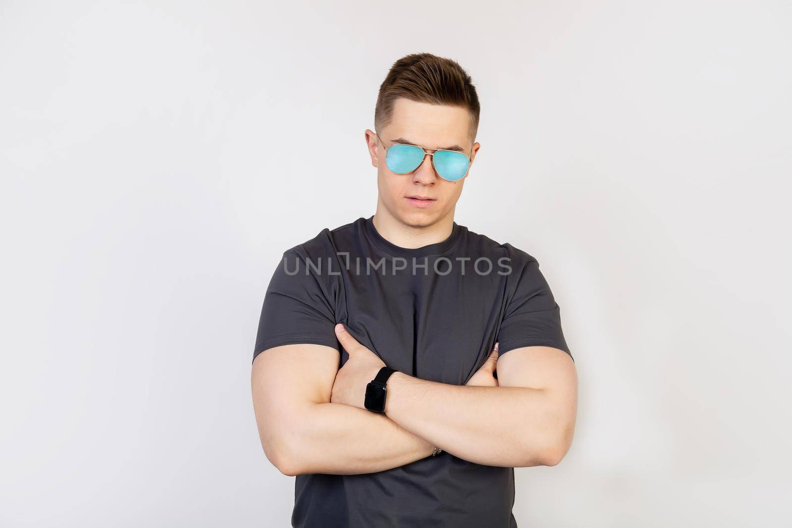 Athletic guy in sunglasses. The young man in sunglasses, frowning in displeasure, holds his hands clasped.