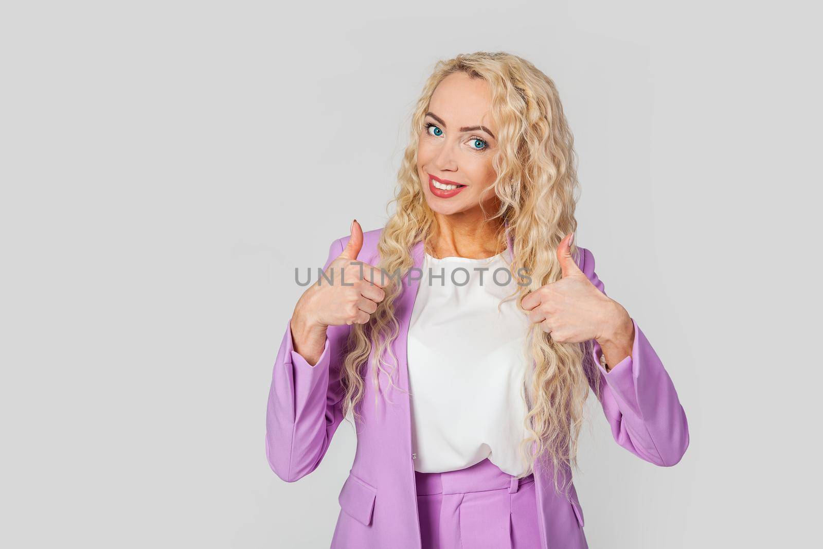 Good job dude, like it. A pleasant beautiful happy blond woman, shows thumb up and smiles broadly, gives a positive review, shares her positive opinion over a gray wall