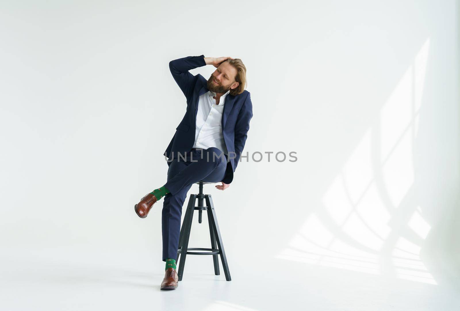A handsome brutal bearded and long-haired man, a stylish businessman sitting on a chair with a white background by vladimirdrozdin