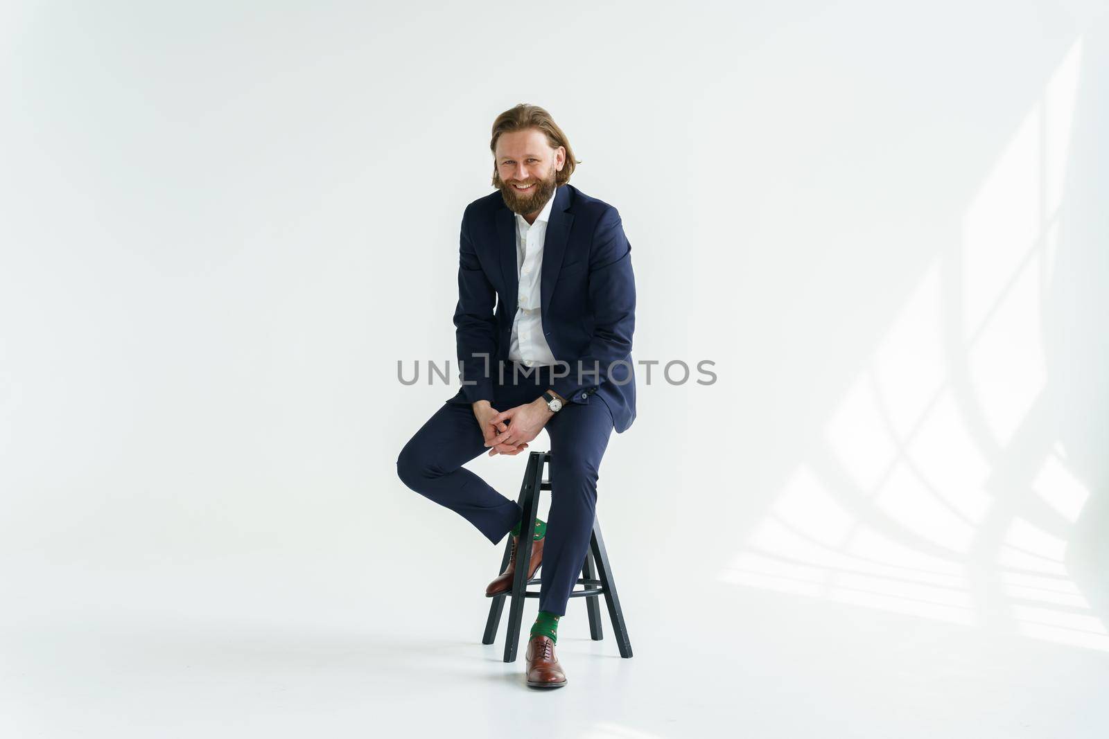 a handsome brutal bearded and long-haired man, a stylish businessman sitting on a chair with a white background. High quality photo