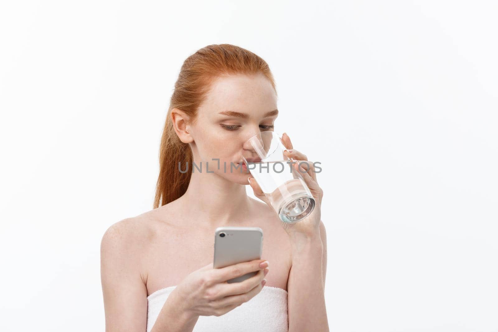 Happy smiling young woman with healthy skin reading and writing in mobile phone sms and drinking clean water. Consulting the diet. Closeup portrait.