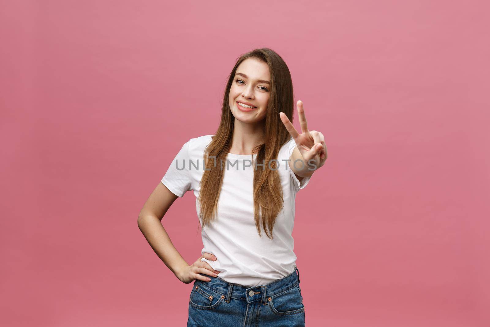 Portrait of a cheerful trendy woman showing two fingers sign over pink background by Benzoix