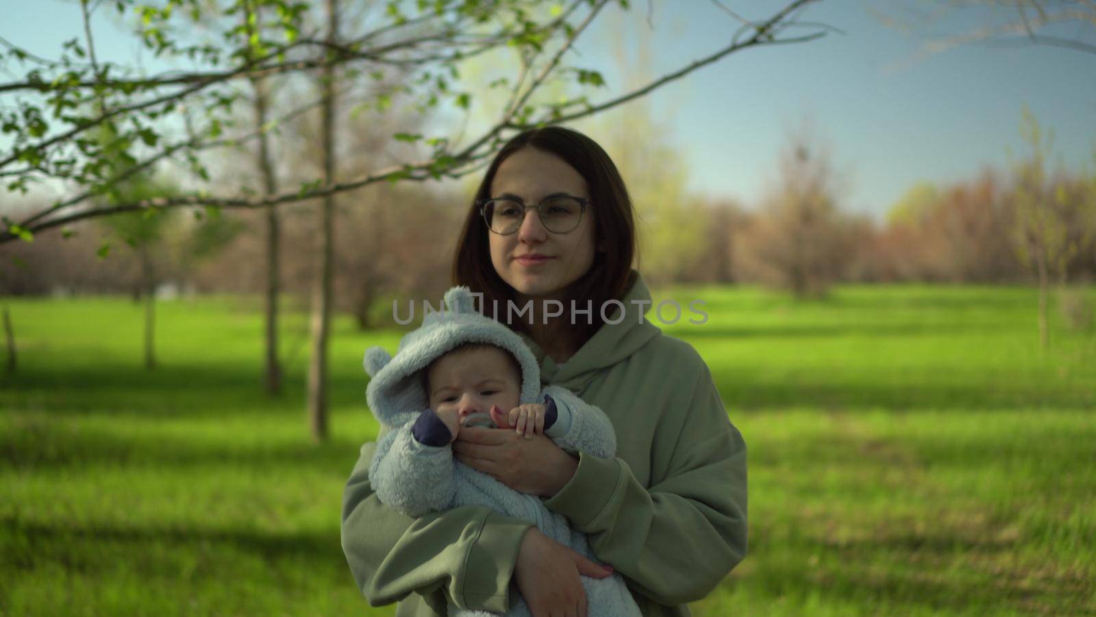 A young mother walks with a baby in nature. A girl with glasses holds a child in her arms. Closeup. 4k