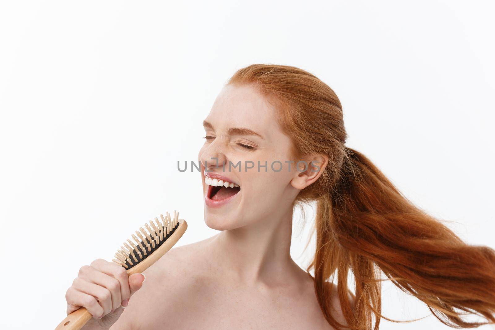 Photo of cheerful smiling freckled ginger young woman combs her long red hair, glad to prepare for date with boyfriend,isolated over white background.