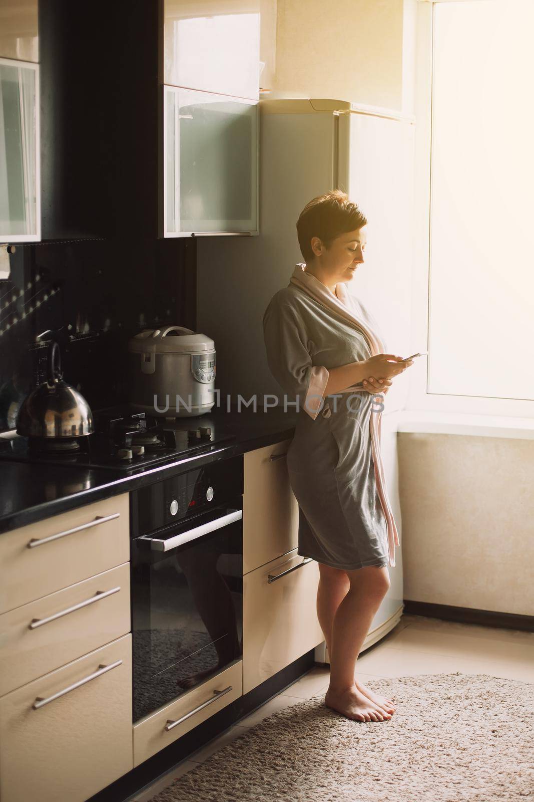 Work from home. Pretty woman in a bathrobe in the kitchen in the morning communications and works on the phone at home. Working at home
