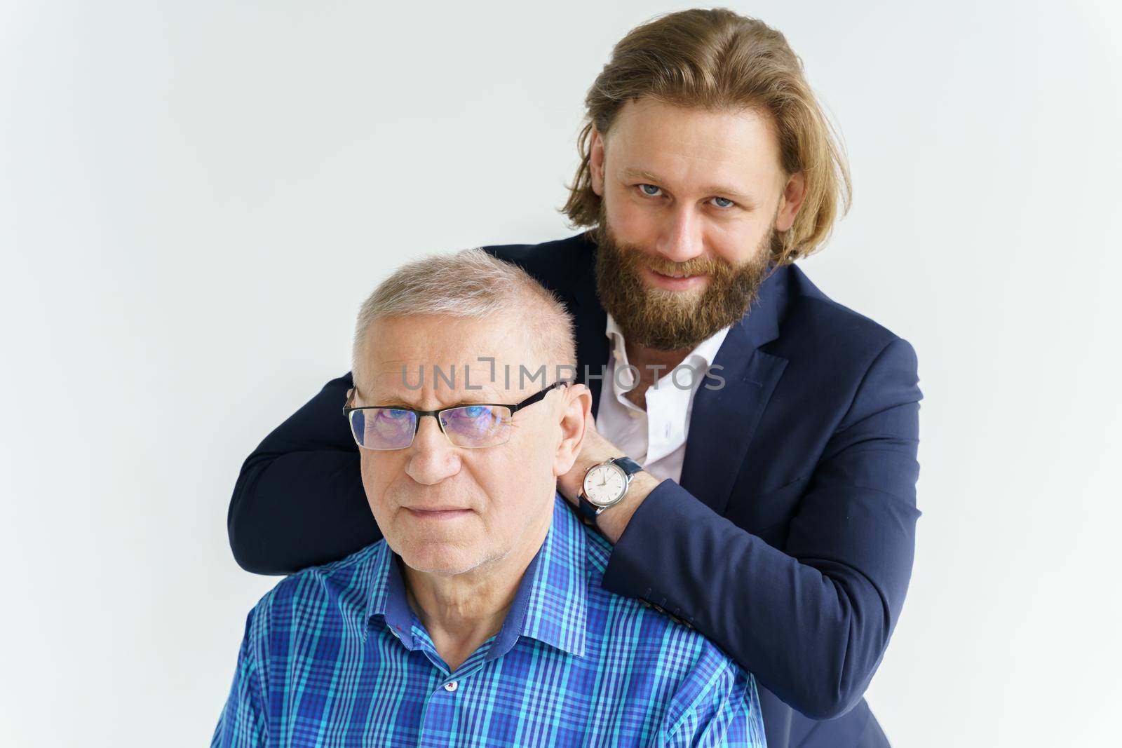 the son in a stylish suit leans on the shoulders of his father, Father and son in white background, both men look into the camera, an elderly man in glasses, young man with a beard and long hair by vladimirdrozdin