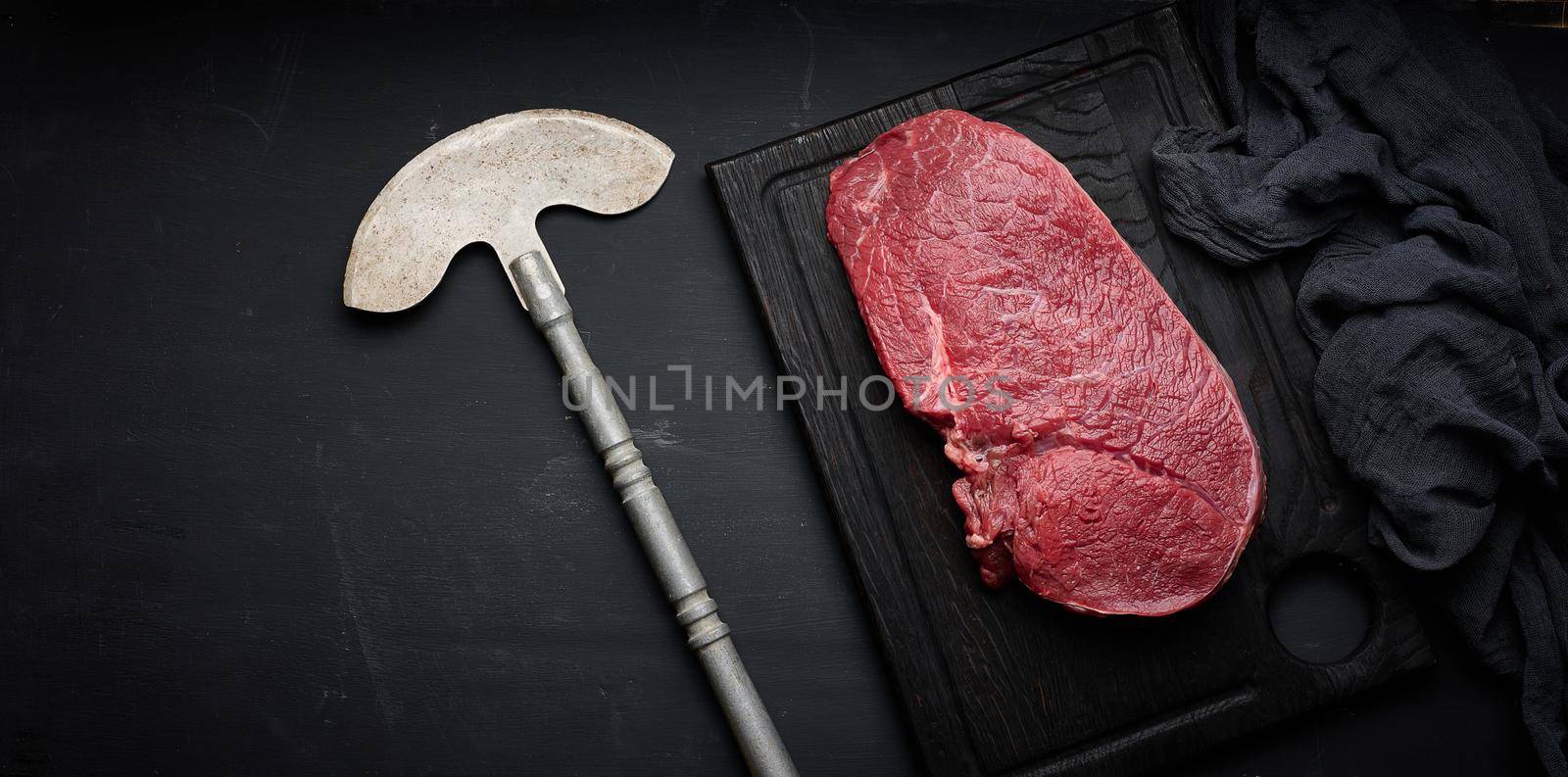 Raw beef tenderloin lies on a cutting board on a black table, top view by ndanko