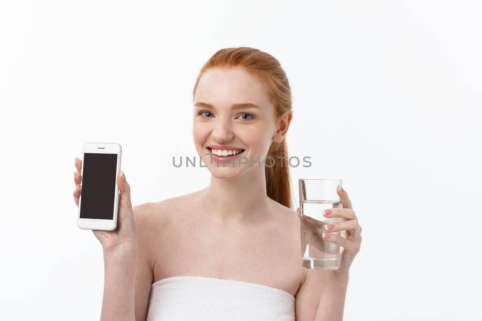 Happy smiling young woman with healthy skin reading and writing in mobile phone sms and drinking clean water. Consulting the diet. Closeup portrait.