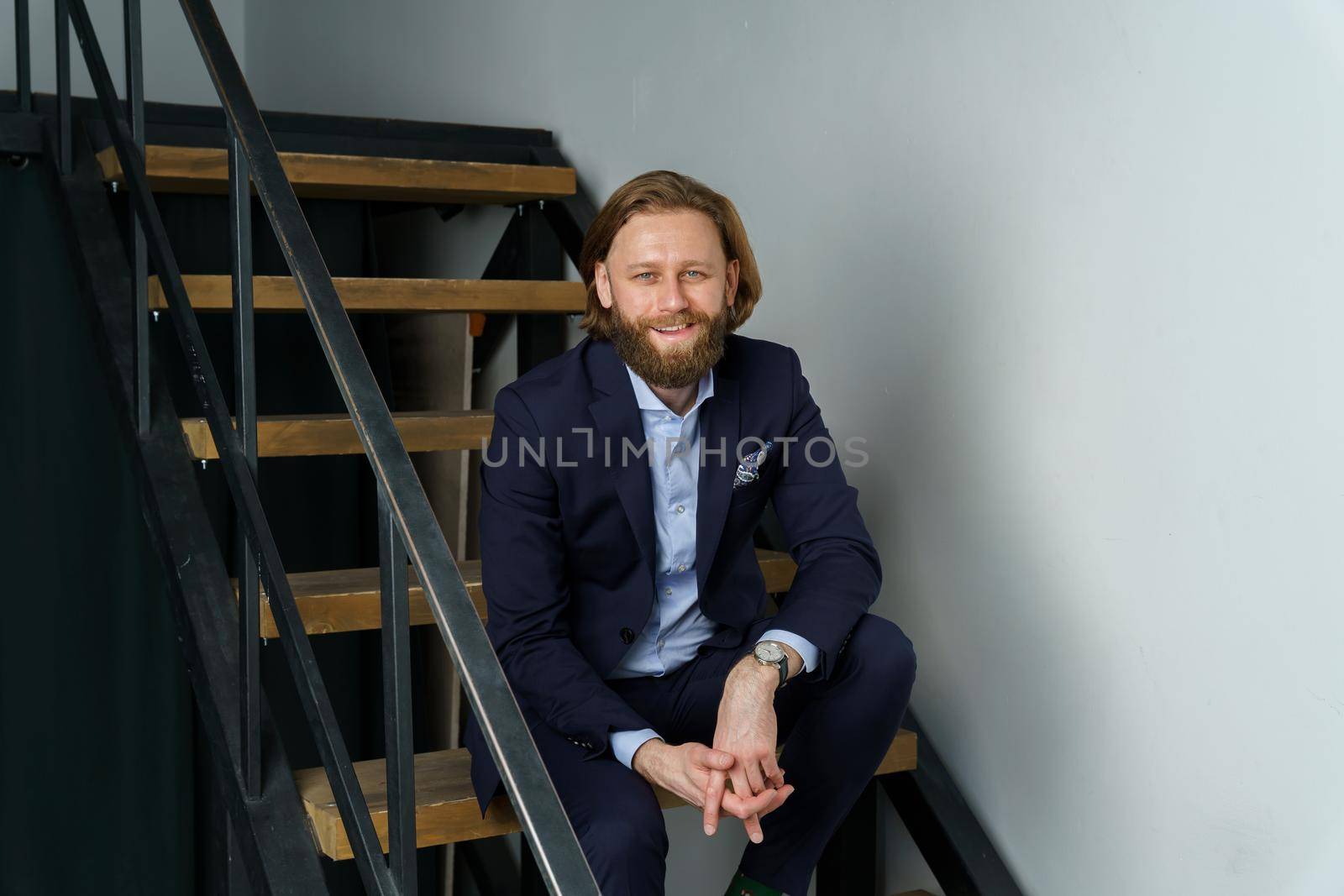 a handsome brutal bearded and long-haired man sits on the steps of the stairs, a stylish businessman by vladimirdrozdin