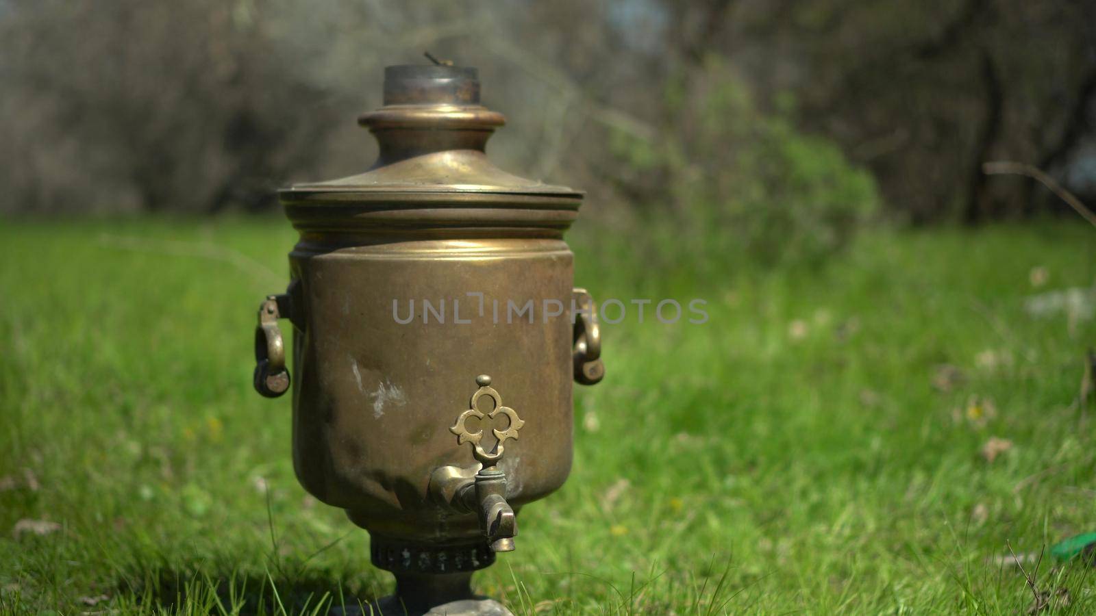 An old bronze samovar stands on the grass at a picnic. 4k