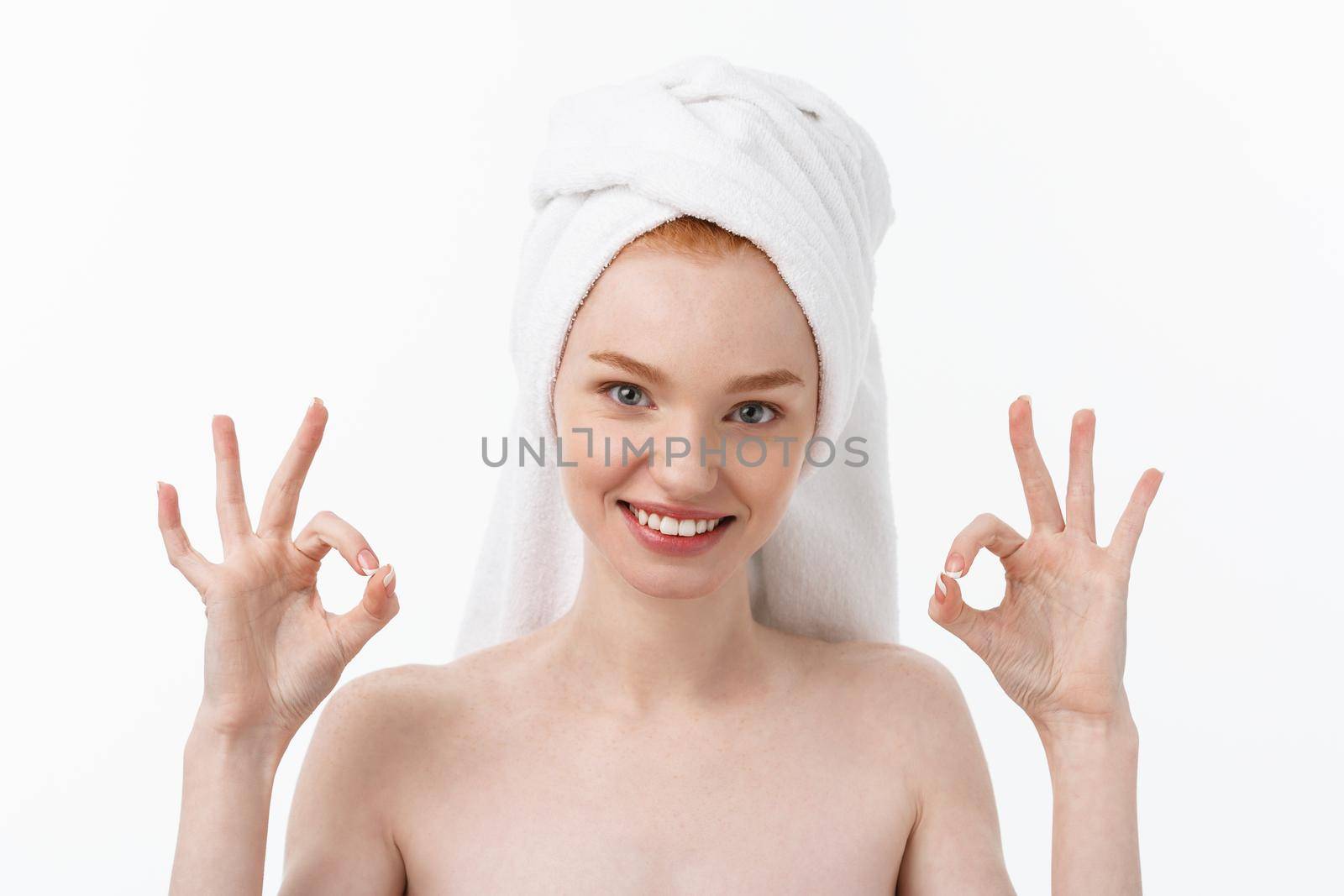 Beauty treatment. Woman applying moisturizing cream skin care product on face, making ok sign studio shot.