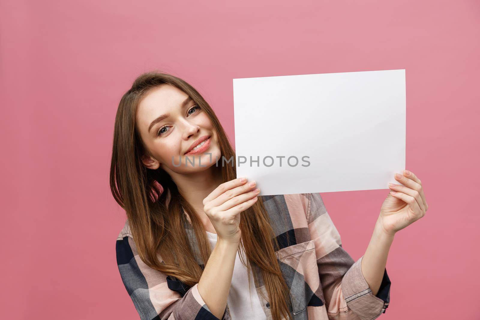 Close up portrait of positive laughing woman smiling and holding white big mockup poster isolated on pink background.