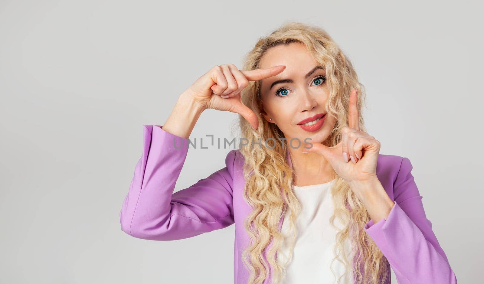 Creative, pretty blonde curly woman, photographer or designer looking for the perfect angle of view from the point of view, making hands framed and smiling
