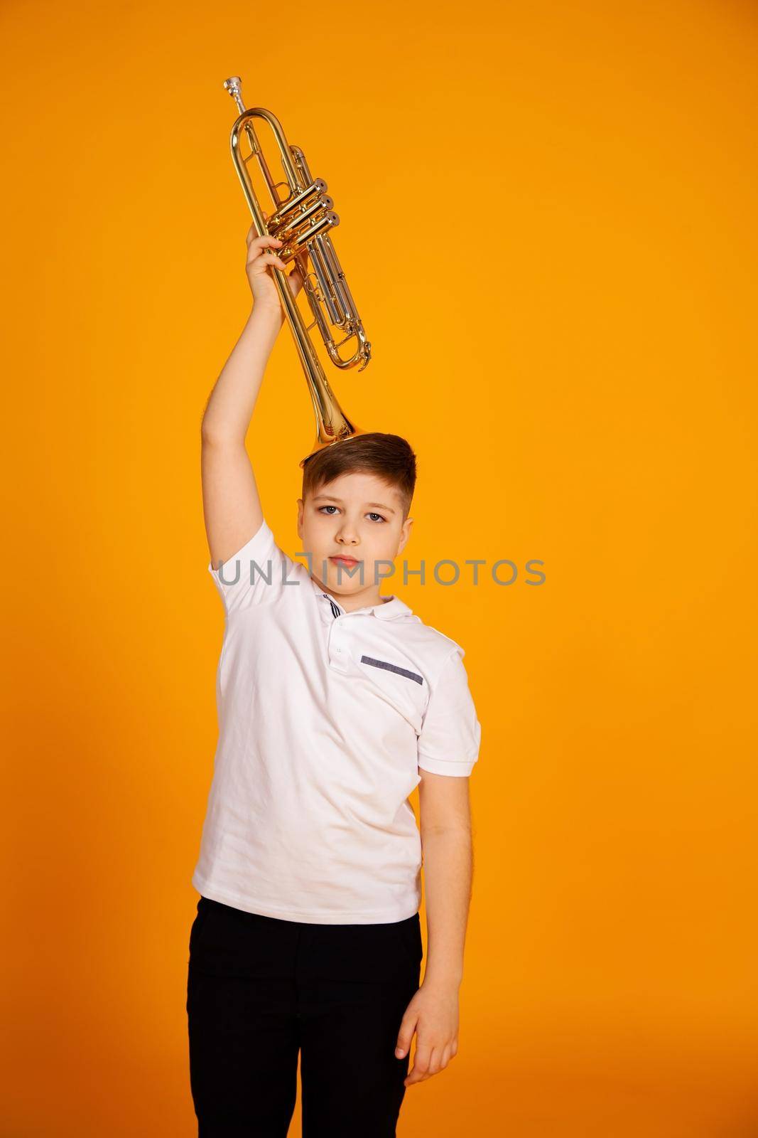 A boy in a white T-shirt holds a trumpet with a musical instrument on his head.