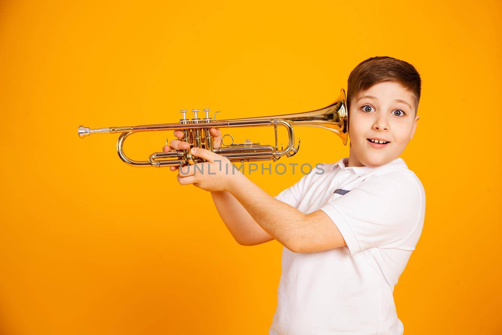 The boy overhears through the pipe. I want to hear everything. Handsome curious boy in a white shirt with a curious expression on his face while spying, eavesdropping, holding a pipe near his ear