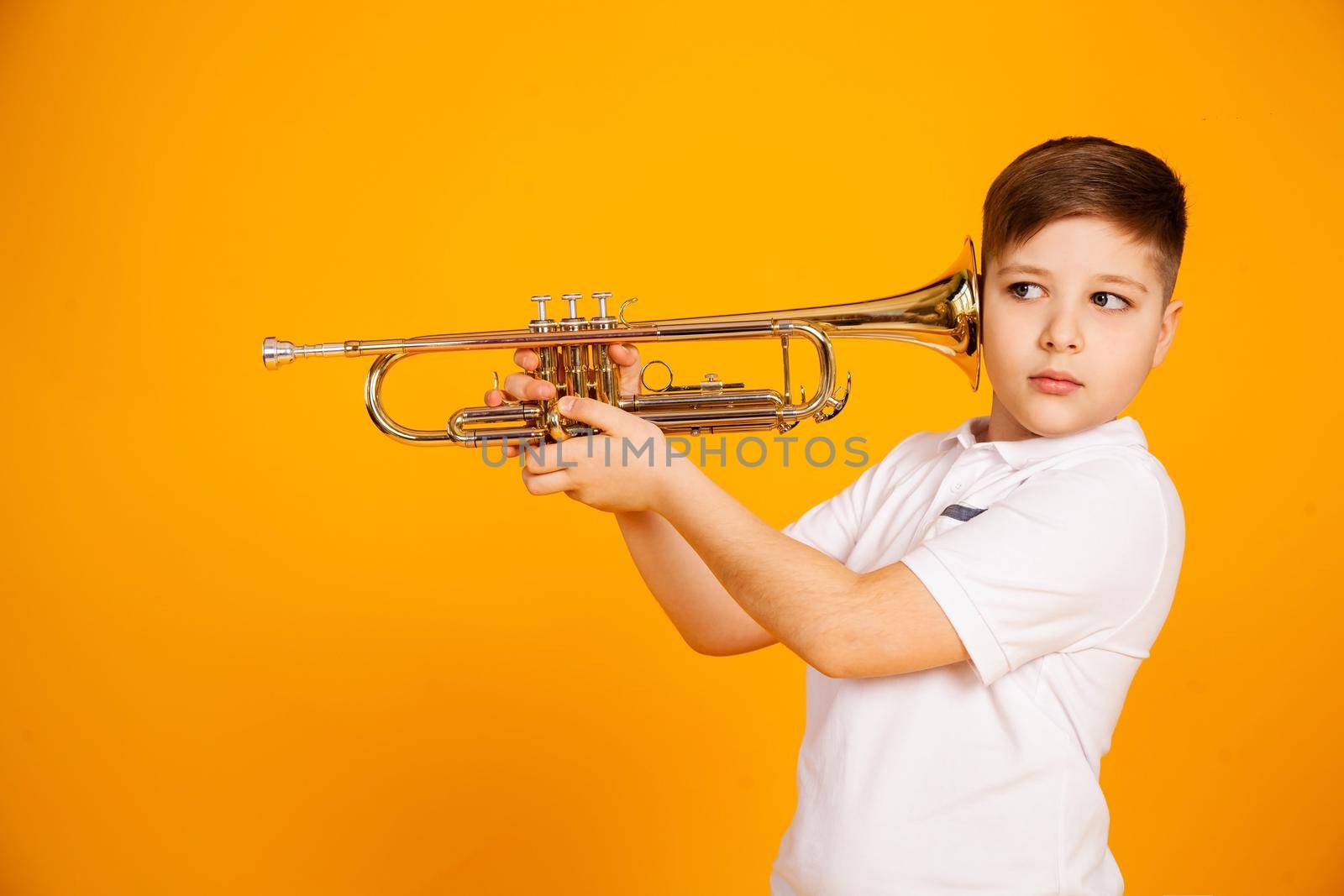 The boy overhears through the pipe. I want to hear everything. Handsome curious boy in a white shirt with a curious expression on his face while spying, eavesdropping, holding a pipe near his ear