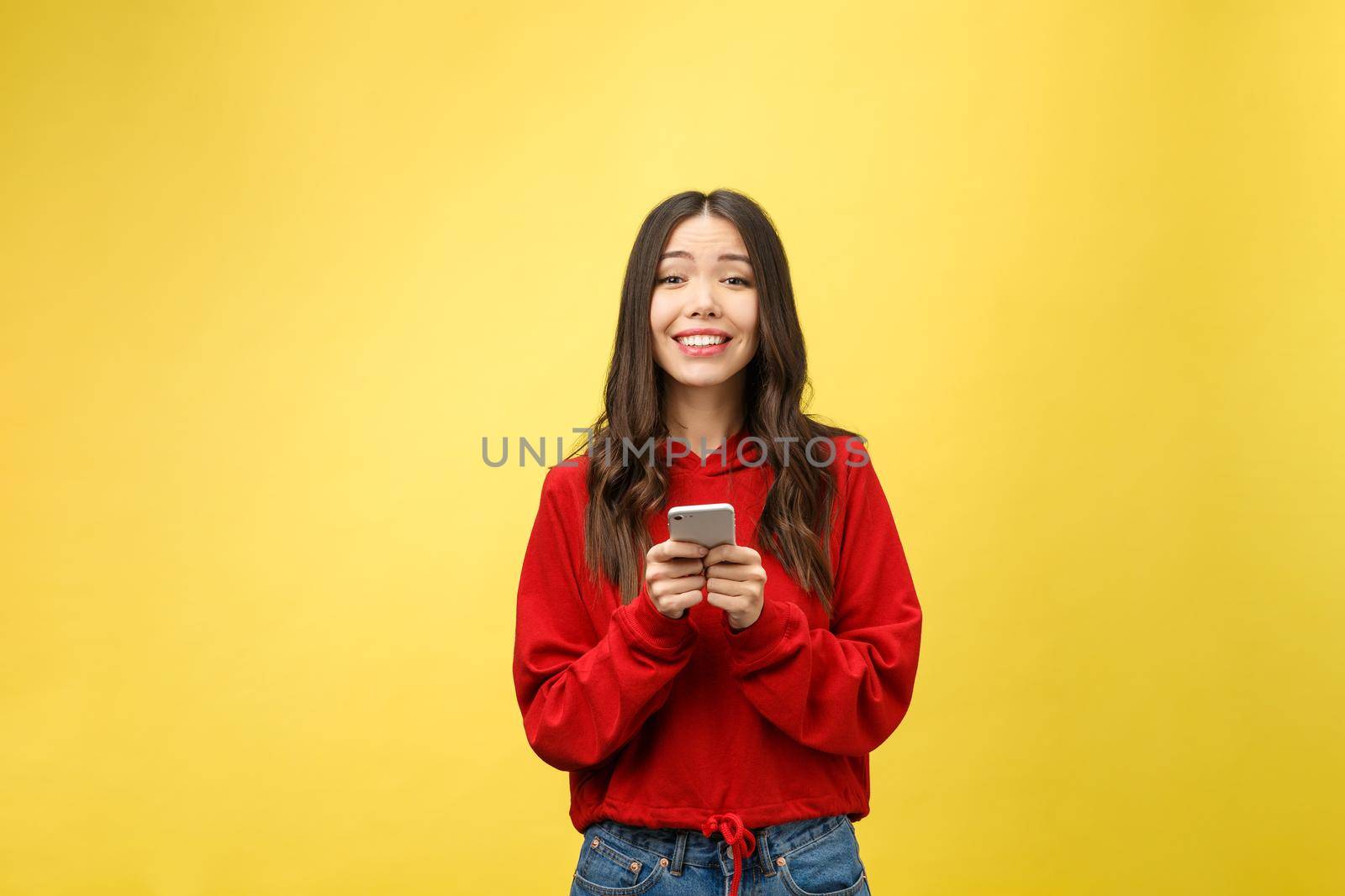 Young beautiful happy woman using smart phone. Isolated on yellow background.