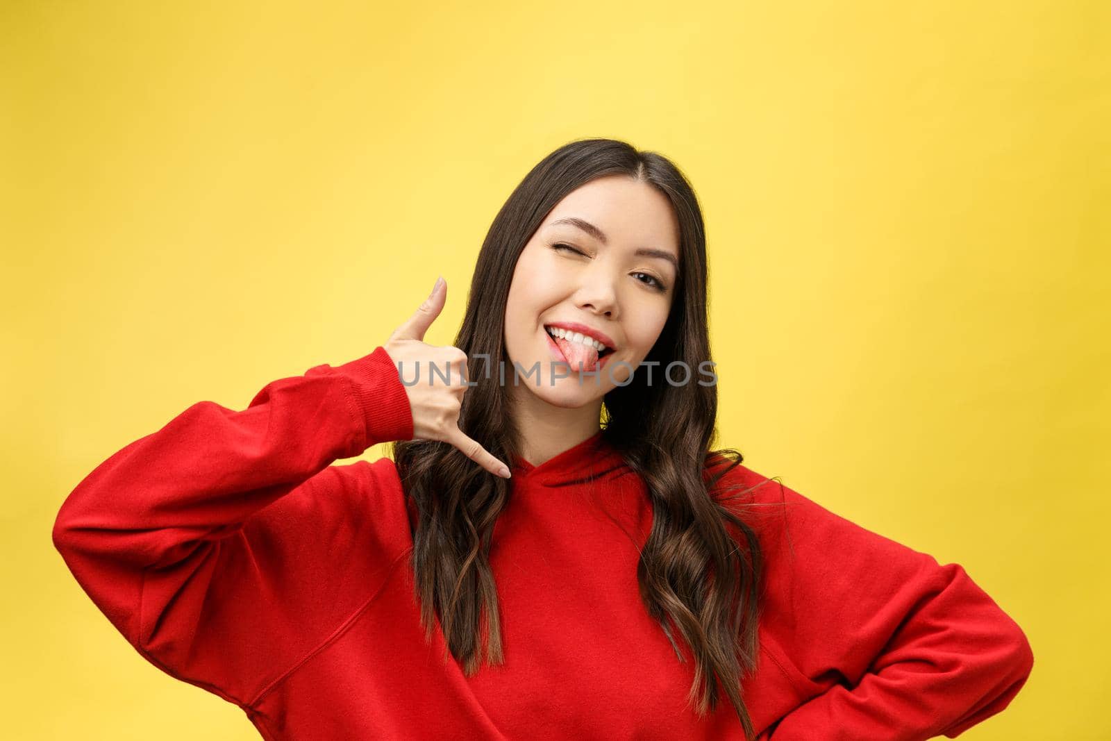 Pretty young woman showing phone sign with her fingers. Colorful studio portrait with yellow background