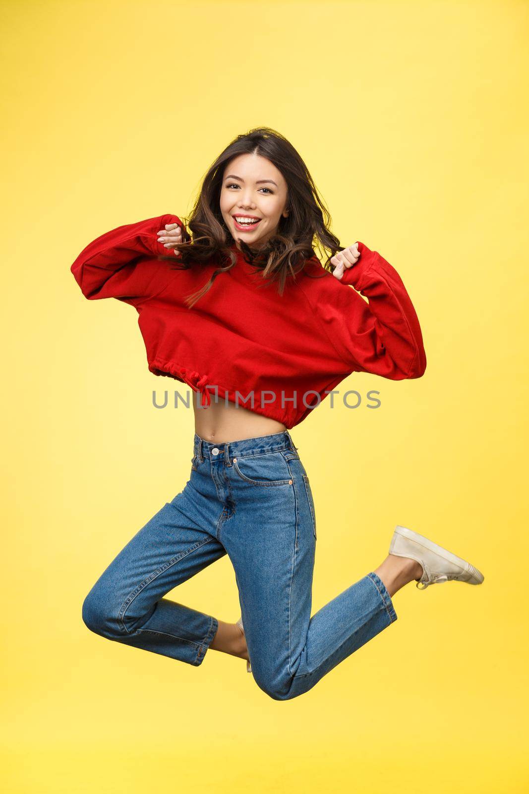 Full length portrait of a smiling pretty woman jumping isolated on a yellow background