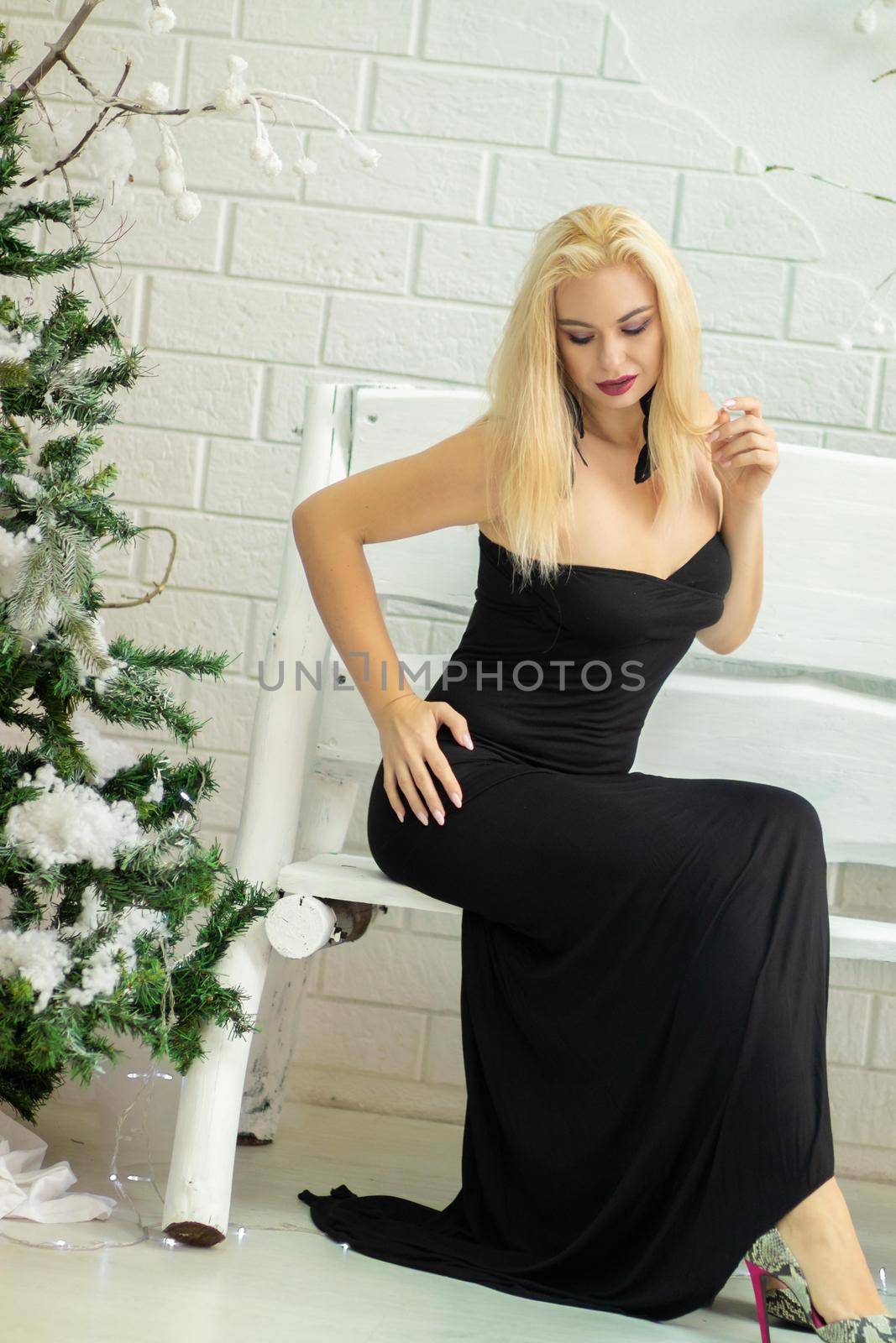 Christmas image with blonde sexy woman in long black dress. Over Christmas decorate and New Year tree