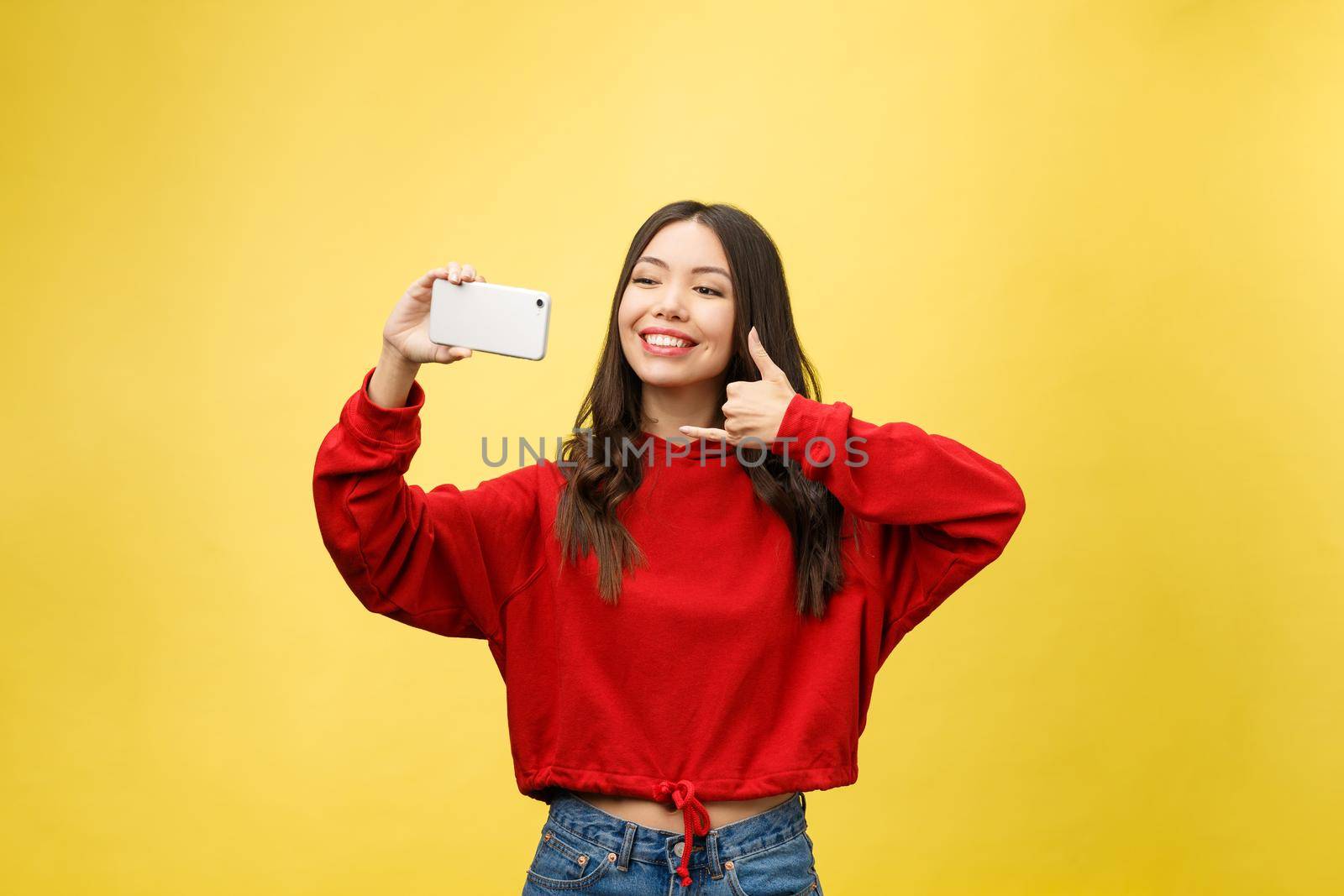 Smiling young girl making selfie photo on smartphone over yellow background.