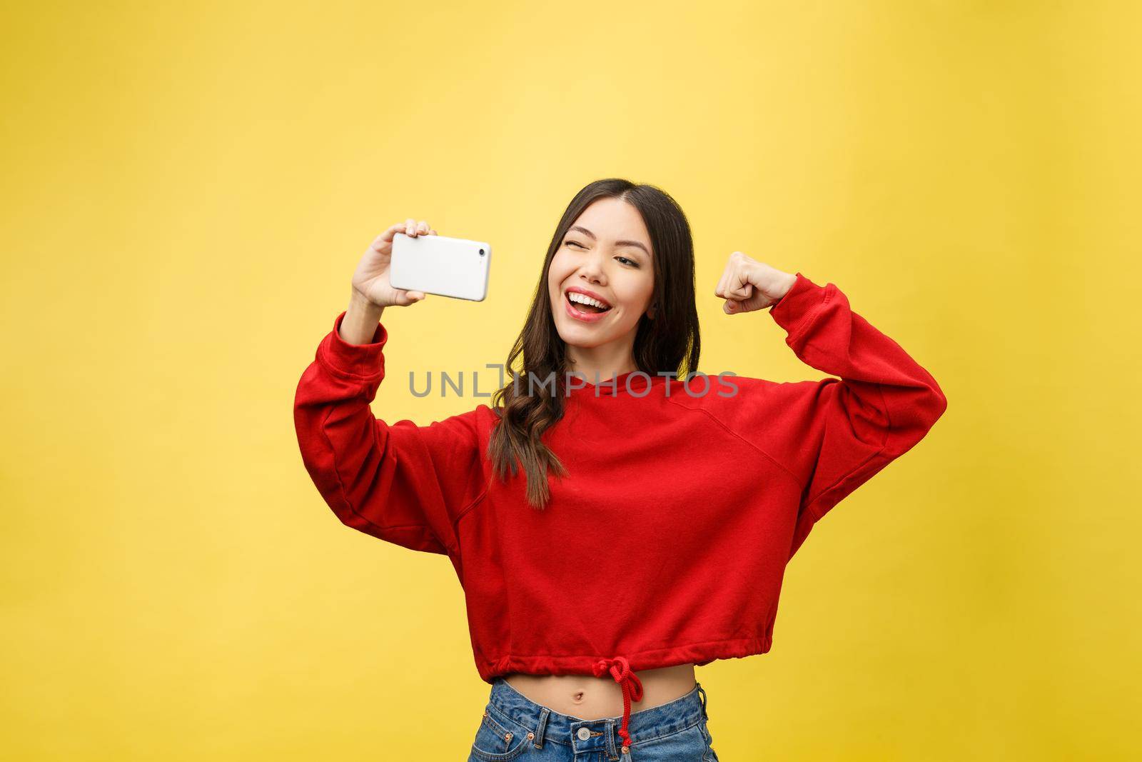 Smiling young girl making selfie photo on smartphone over yellow background by Benzoix