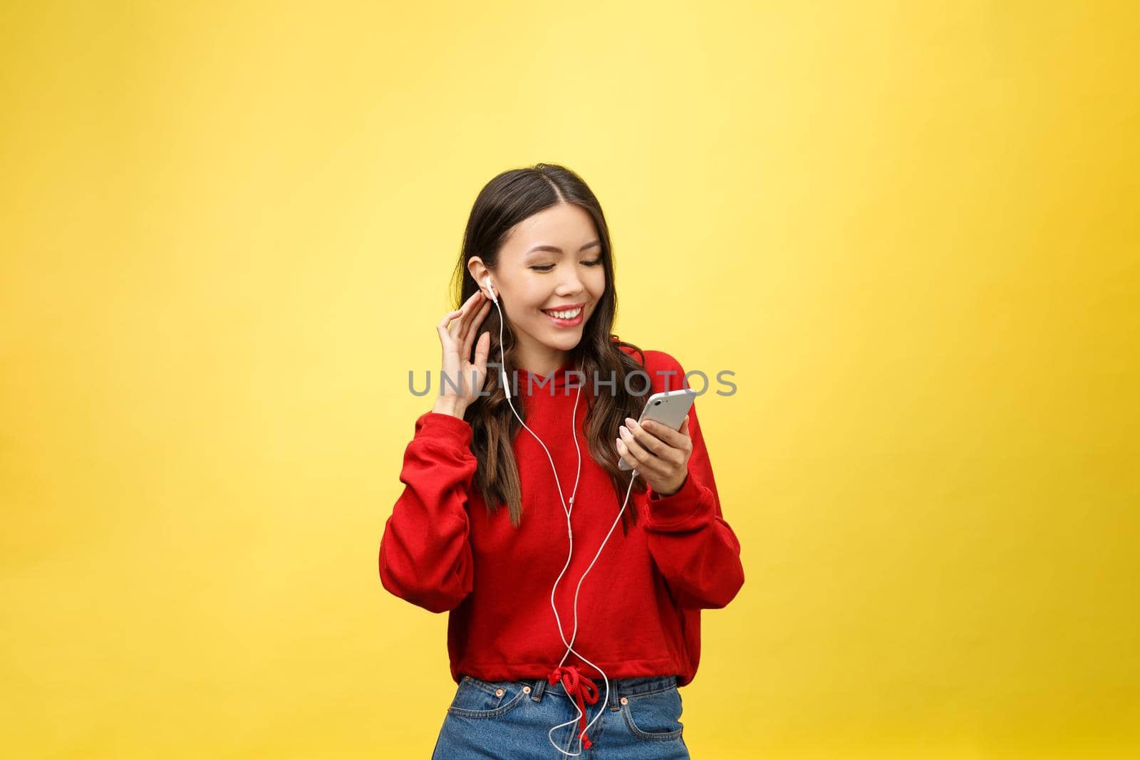 Portrait of a happy woman listening music in earphones and dancing isolated on a yellow background.