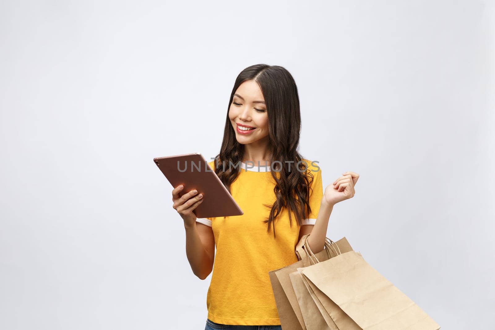 Portrait of woman in summer dress holding packages bags with purchases after online shopping, using tablet pc pad computer isolated on white background. Copy space for advertisement by Benzoix