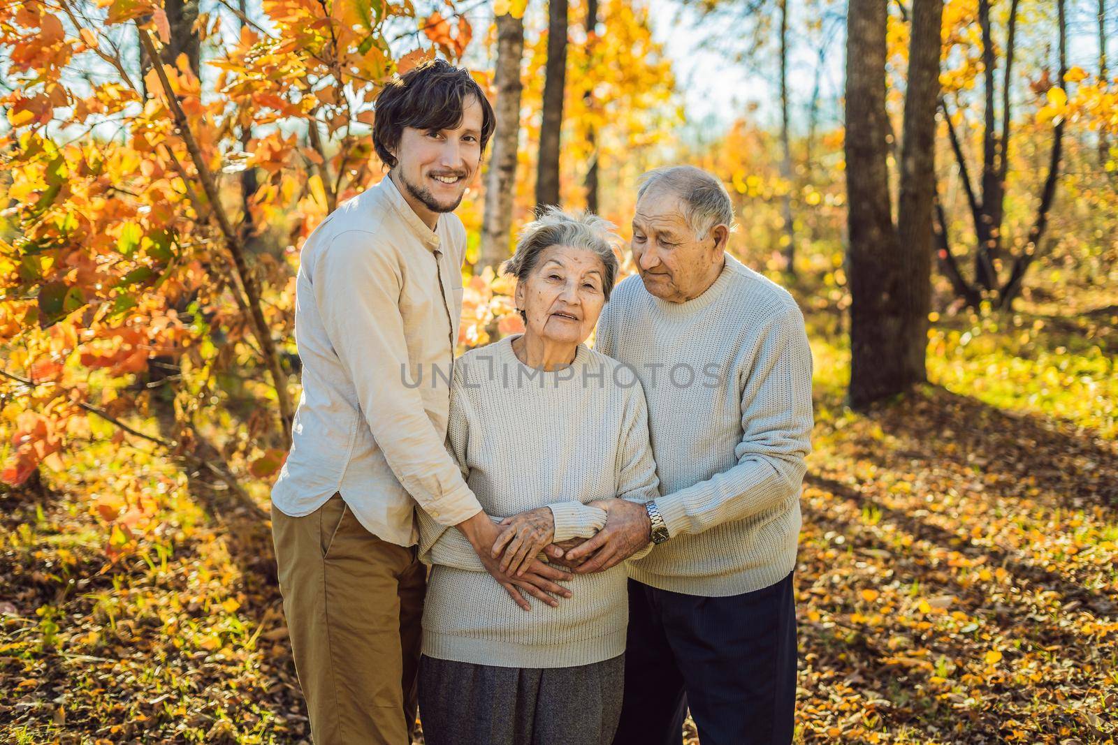 Grandmother, grandfather and adult grandson hugging in autumn park.
