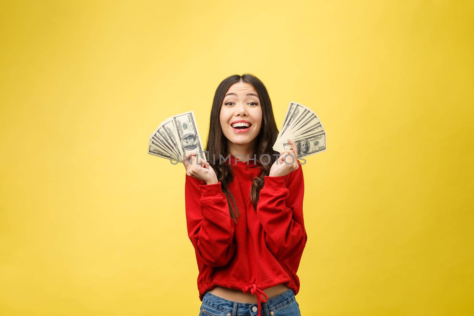 Closeup of young beautiful woman with us dollar money in hand over yellow background, with copy space.