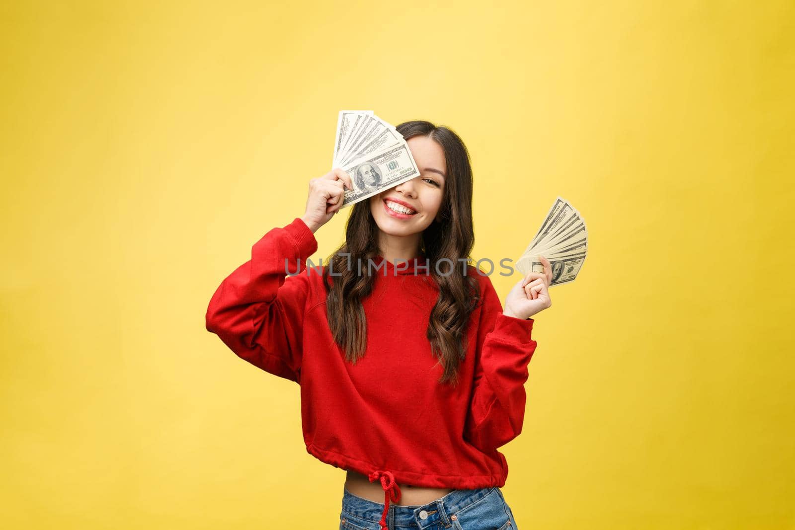 Closeup of young beautiful woman with us dollar money in hand over yellow background, with copy space.