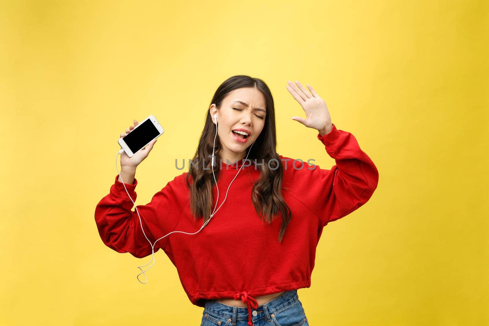 Portrait of a happy woman listening music in earphones and dancing isolated on a yellow background by Benzoix