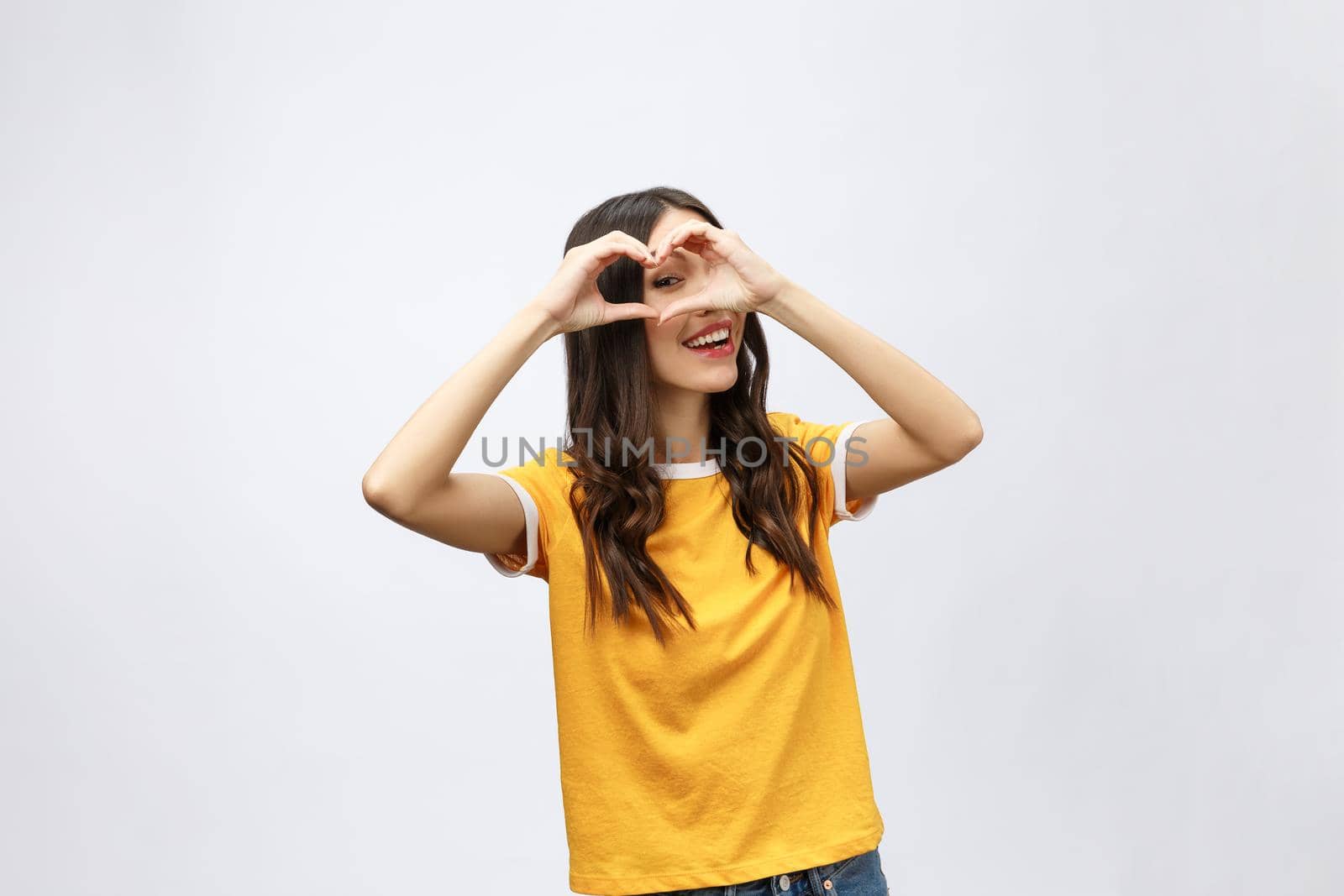 Portrait of a smiling young asian woman showing heart gesture with two hands and looking at camera isolated over white background. by Benzoix