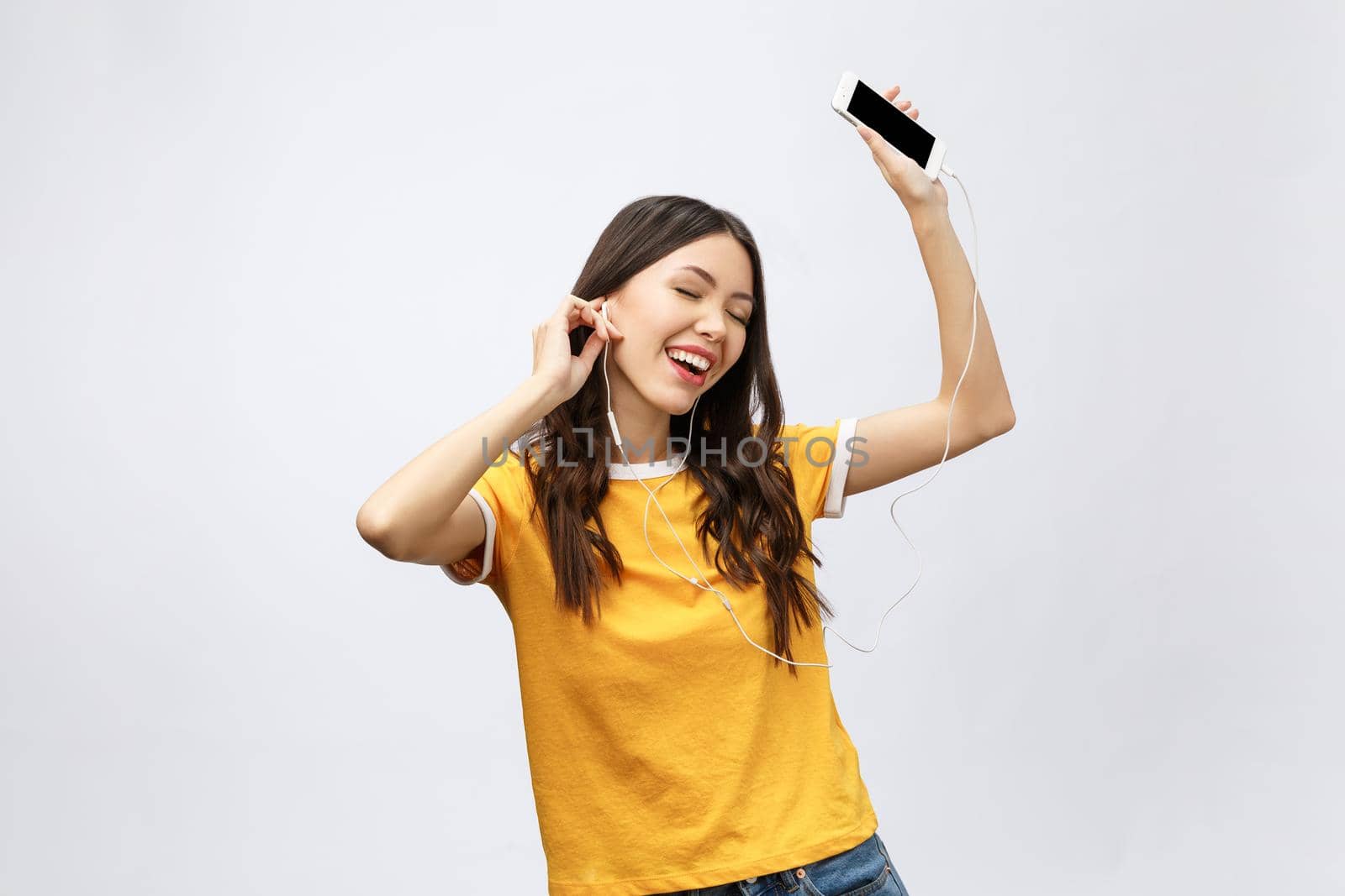 Beautiful asian girl with professional makeup and stylish hairstyle singing and dancing while listening to music on grey background