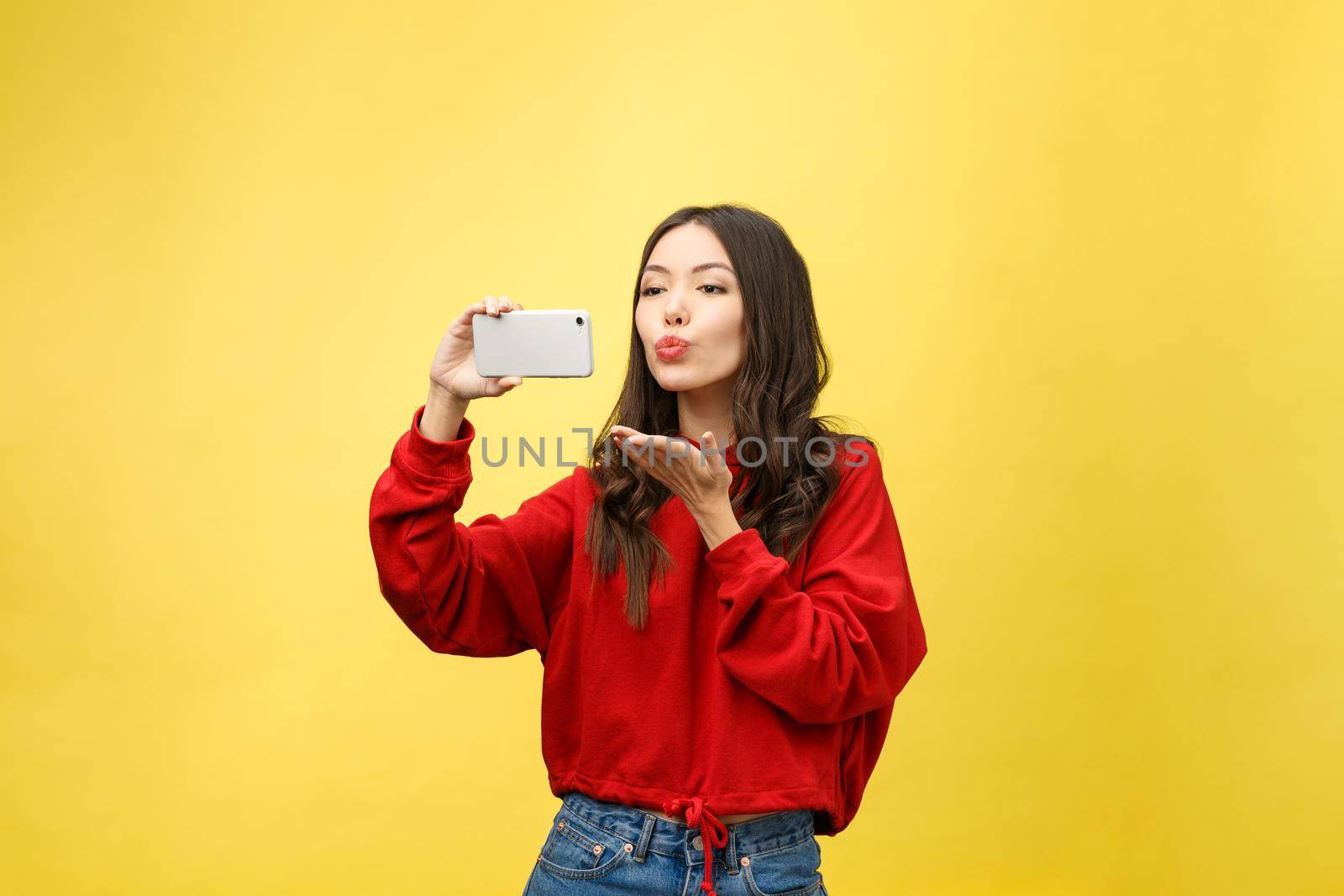 Smiling young girl making selfie photo on smartphone over yellow background.