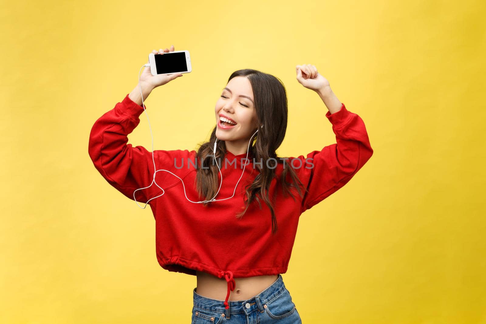 Portrait of a happy woman listening music in earphones and dancing isolated on a yellow background.