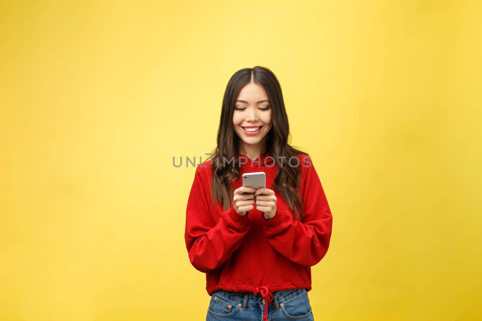 Young beautiful happy woman using smart phone. Isolated on yellow background.