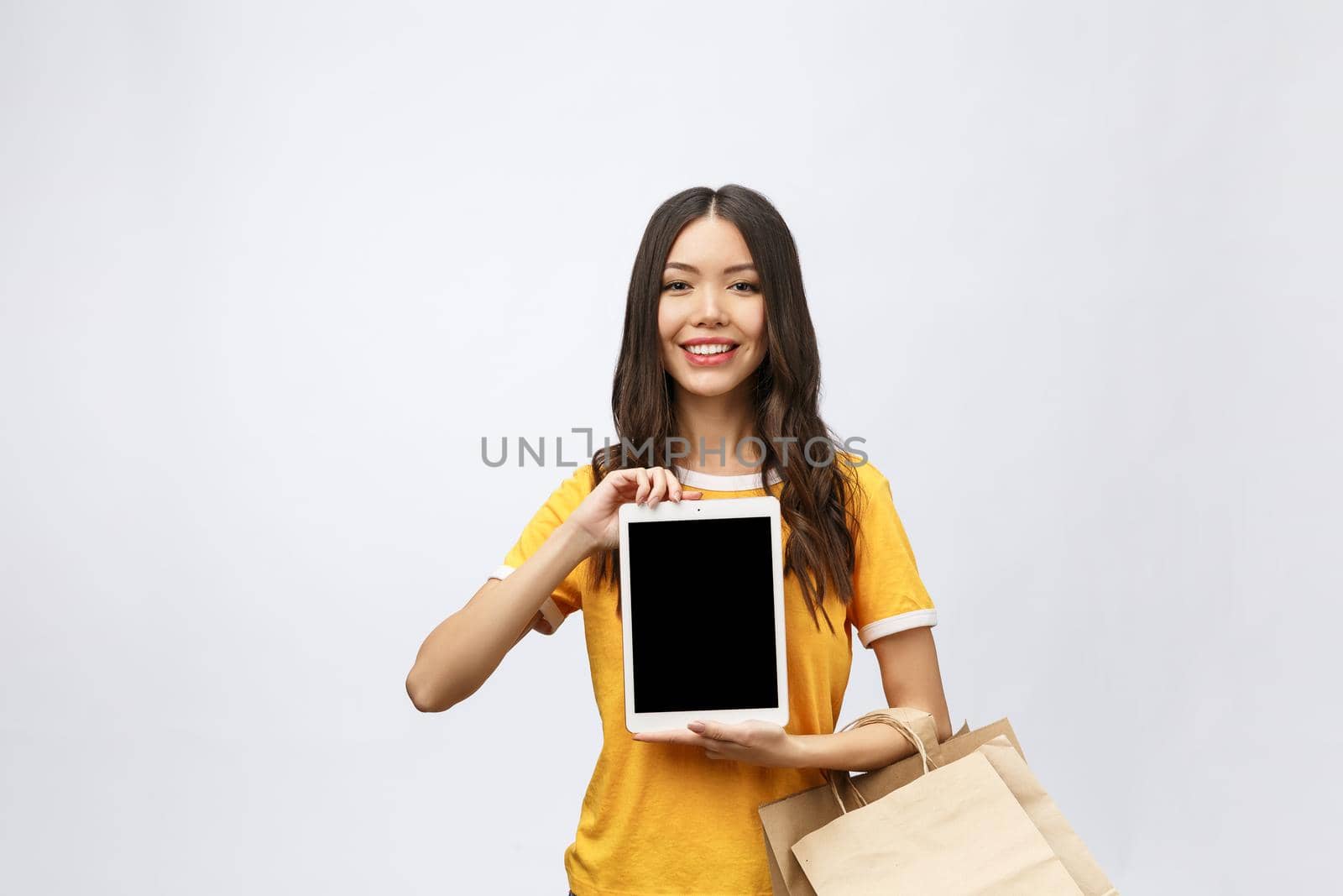 Portrait of woman in summer dress holding packages bags with purchases after online shopping, using tablet pc pad computer isolated on white background. Copy space for advertisement.