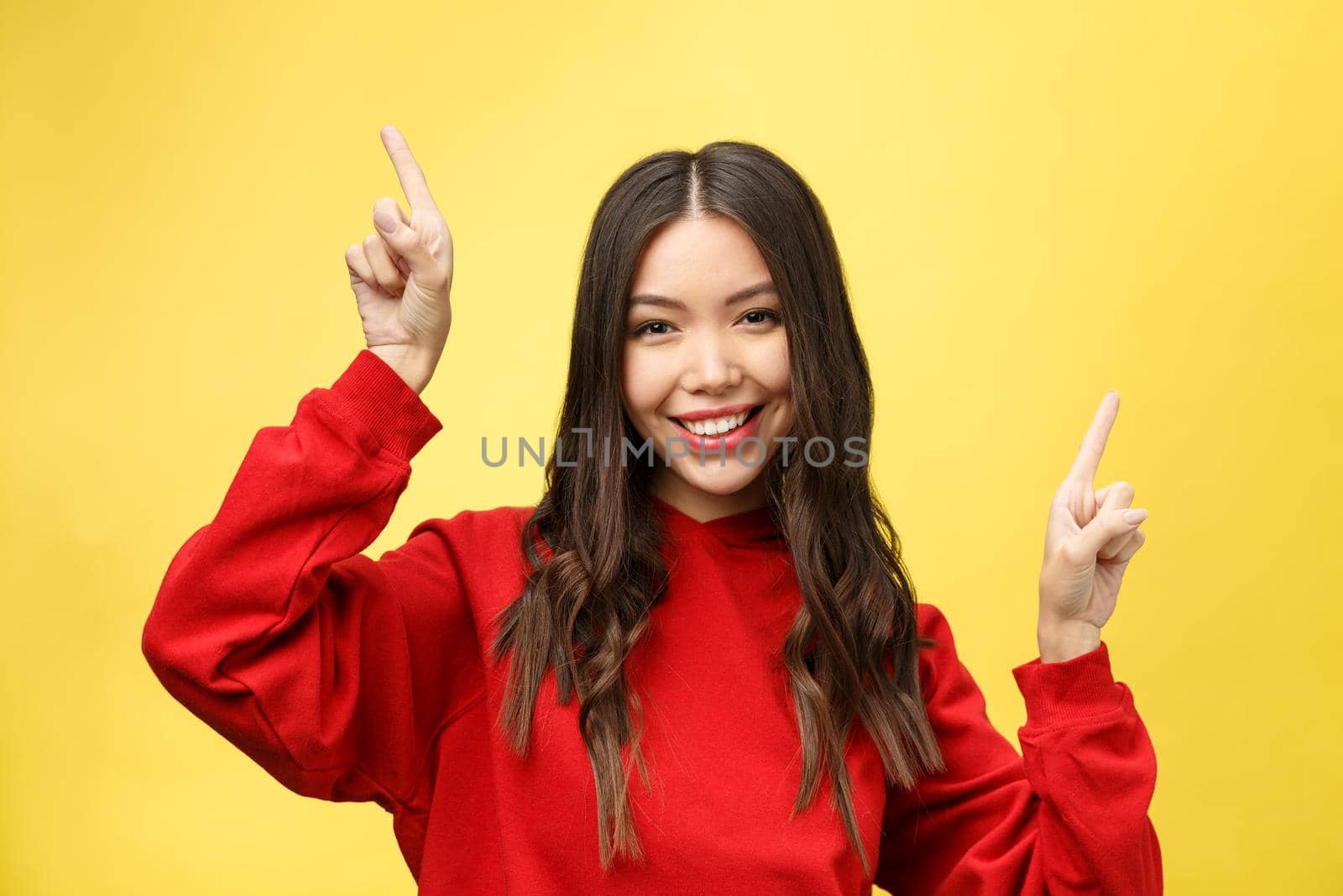 Young beautiful asian woman pointing to copyspace, isolated on yellow background.