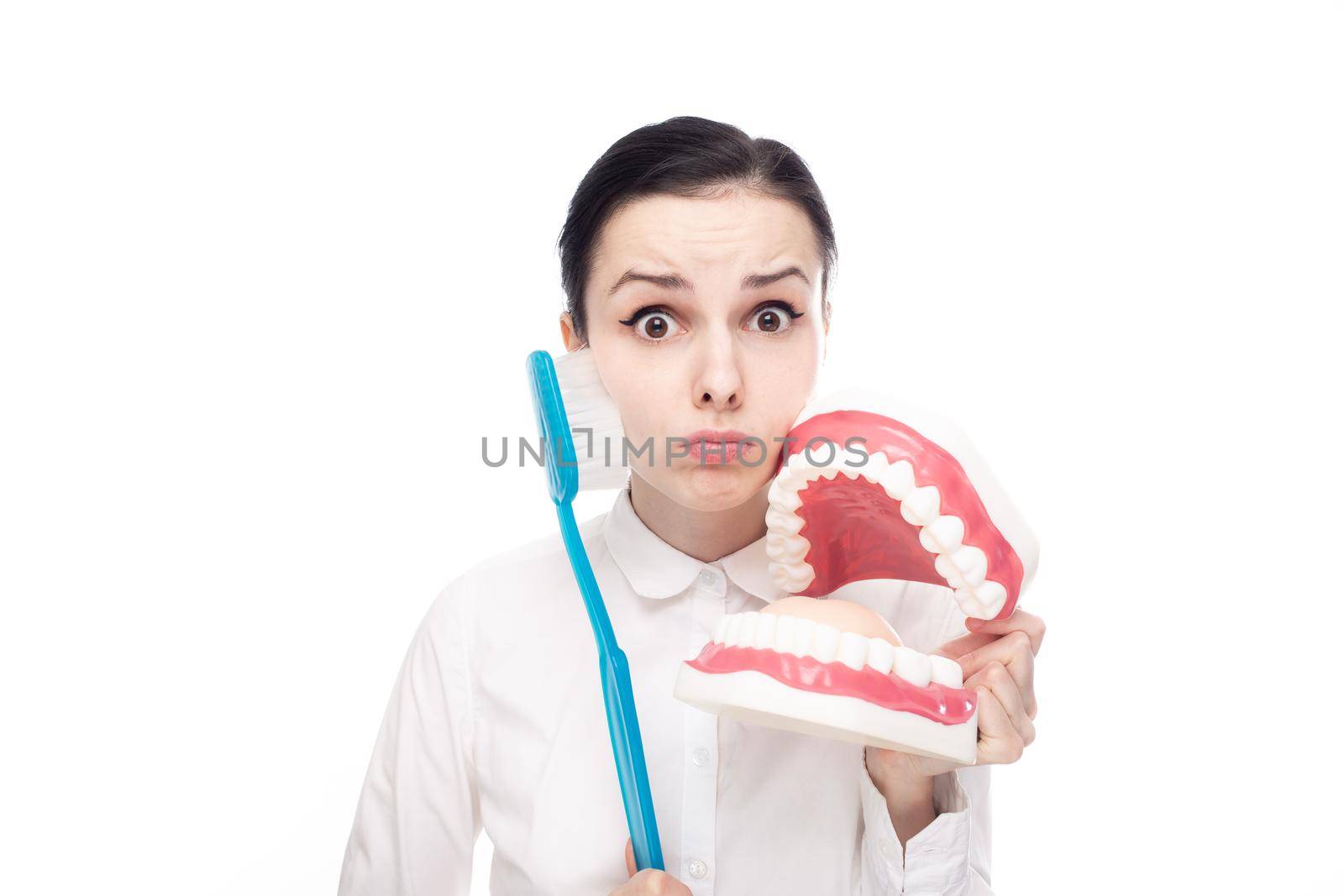 surprised woman in white shirt holding giant toothbrush and dental jaw mockup. High quality photo