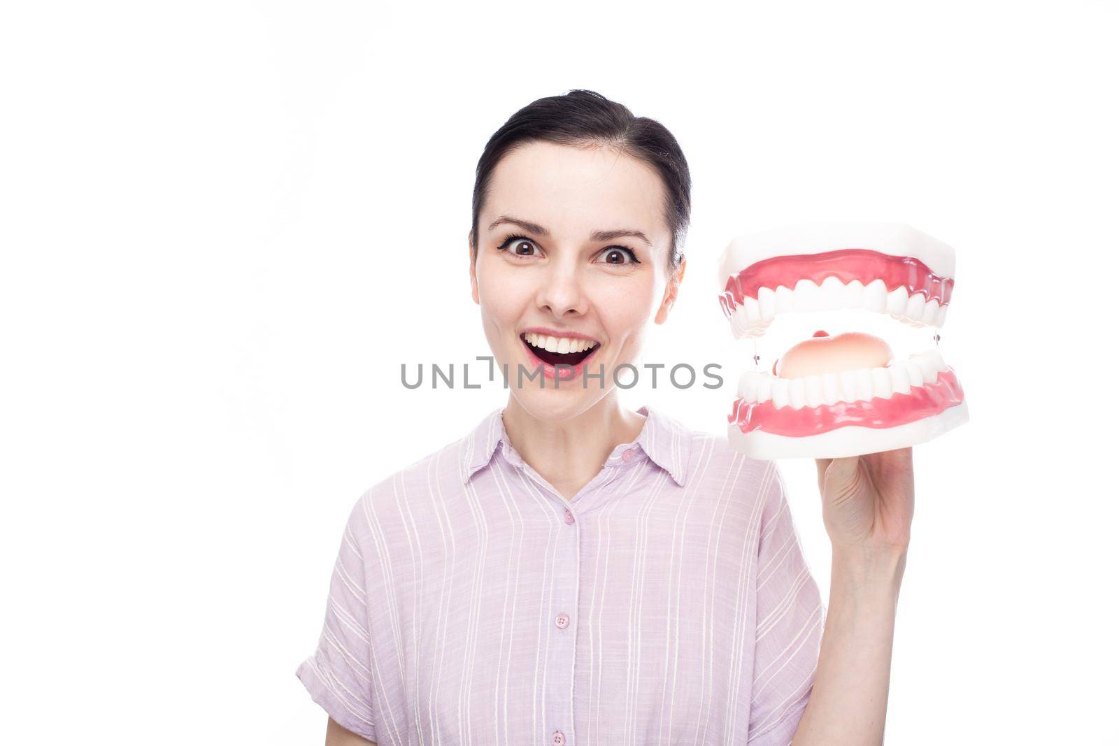 surprised woman in a purple shirt holds a huge jaw mockup in her hand, white background by shilovskaya